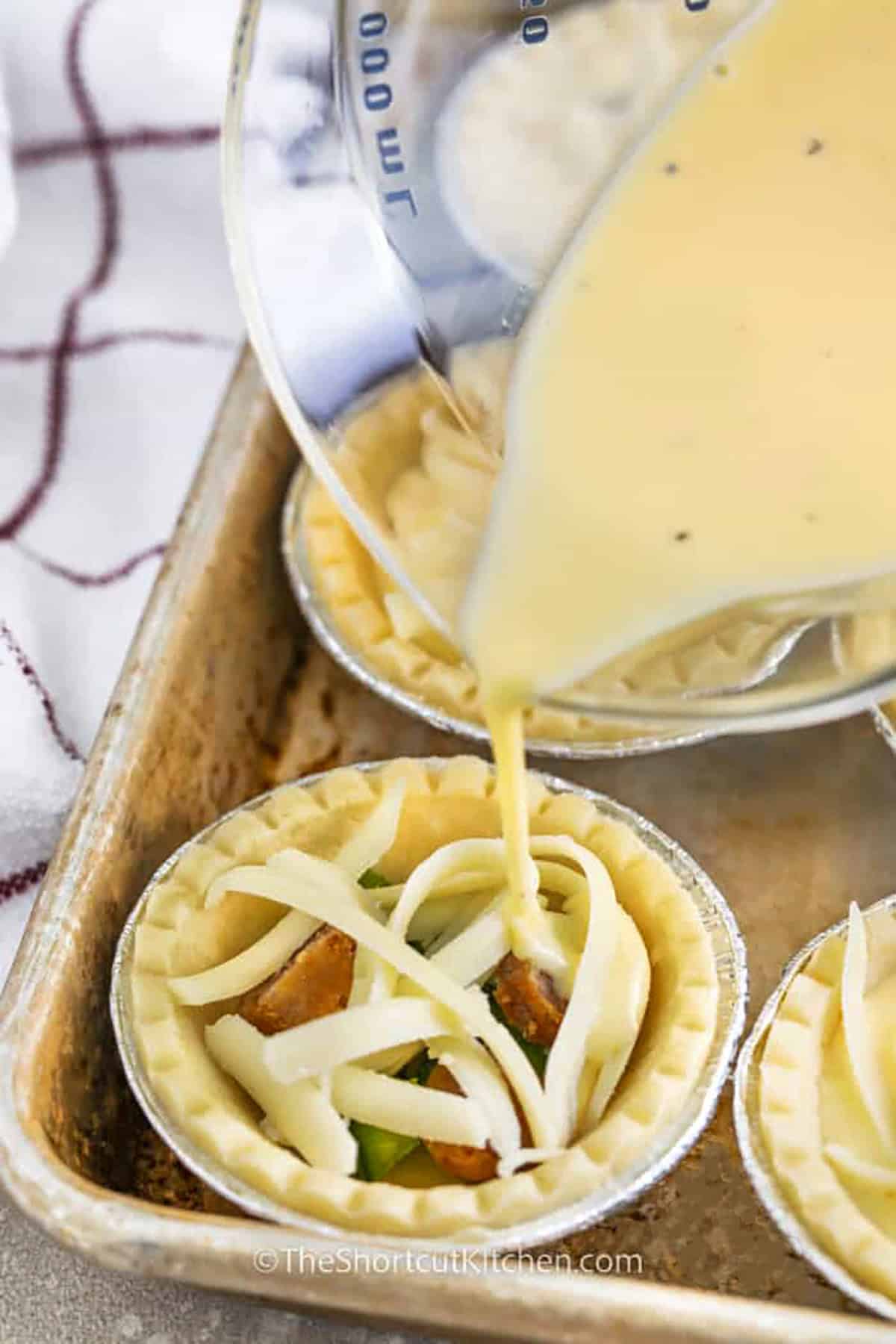 adding egg to tart shells with filling to make Mini Quiches