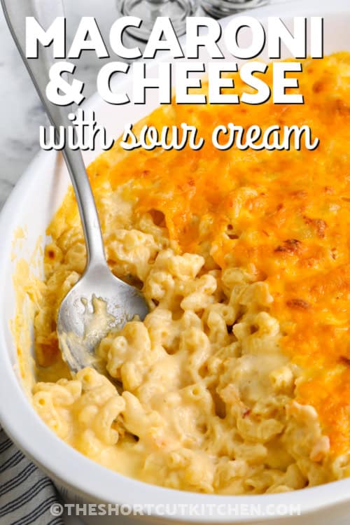 A serving of mac and cheese with sour cream being scooped out of a casserole dish with a title