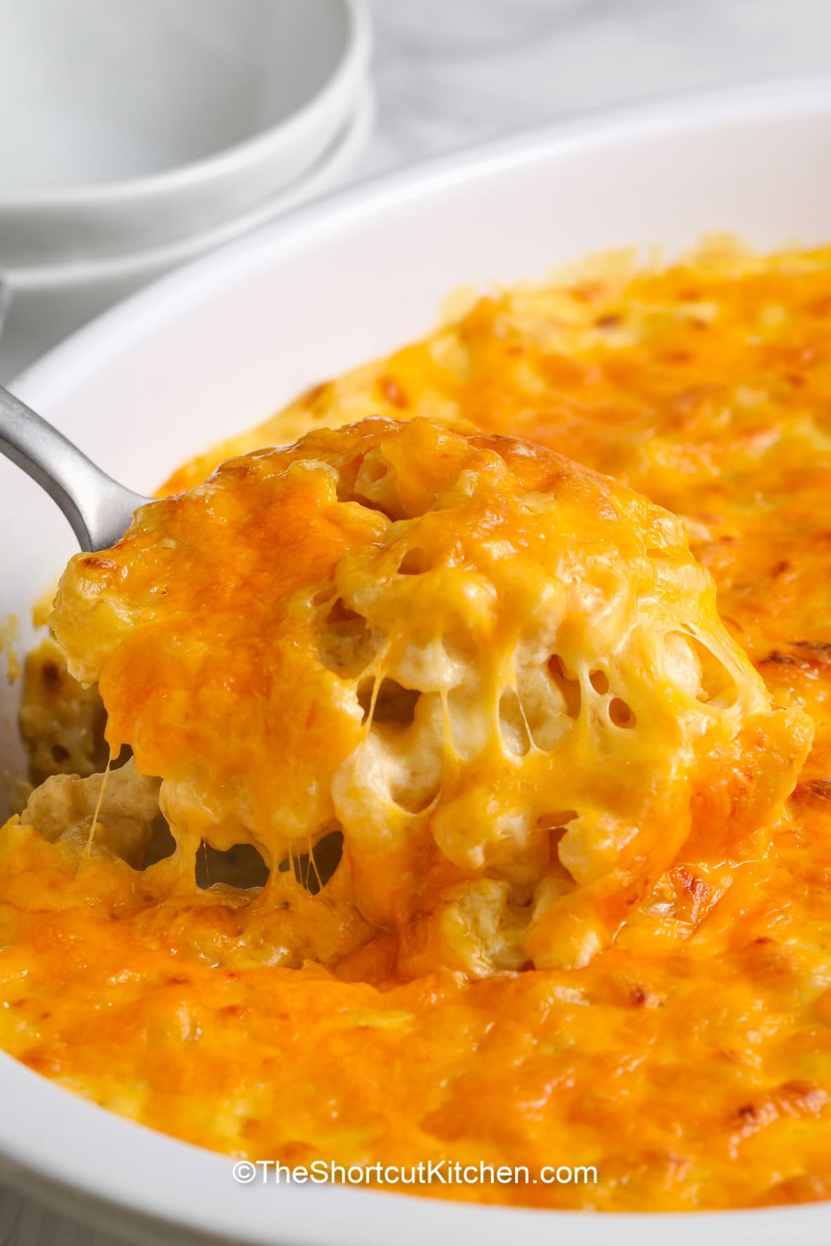 This easy homemade macaroni and cheese with sour cream is the best comfort food! With a creamy sauce made from milk, cheddar, and sour cream, it's a cheesy delight. The recipe comes together quickly, blending creamy flavors with a rich, golden-baked top. Perfect for any occasion, this cheesy, oven-baked dish is sure to satisfy cravings for a warm, delicious, and comforting meal. A true crowd-pleaser! #theshortcutkitchen a scoop of sour cream macaroni and cheese being served