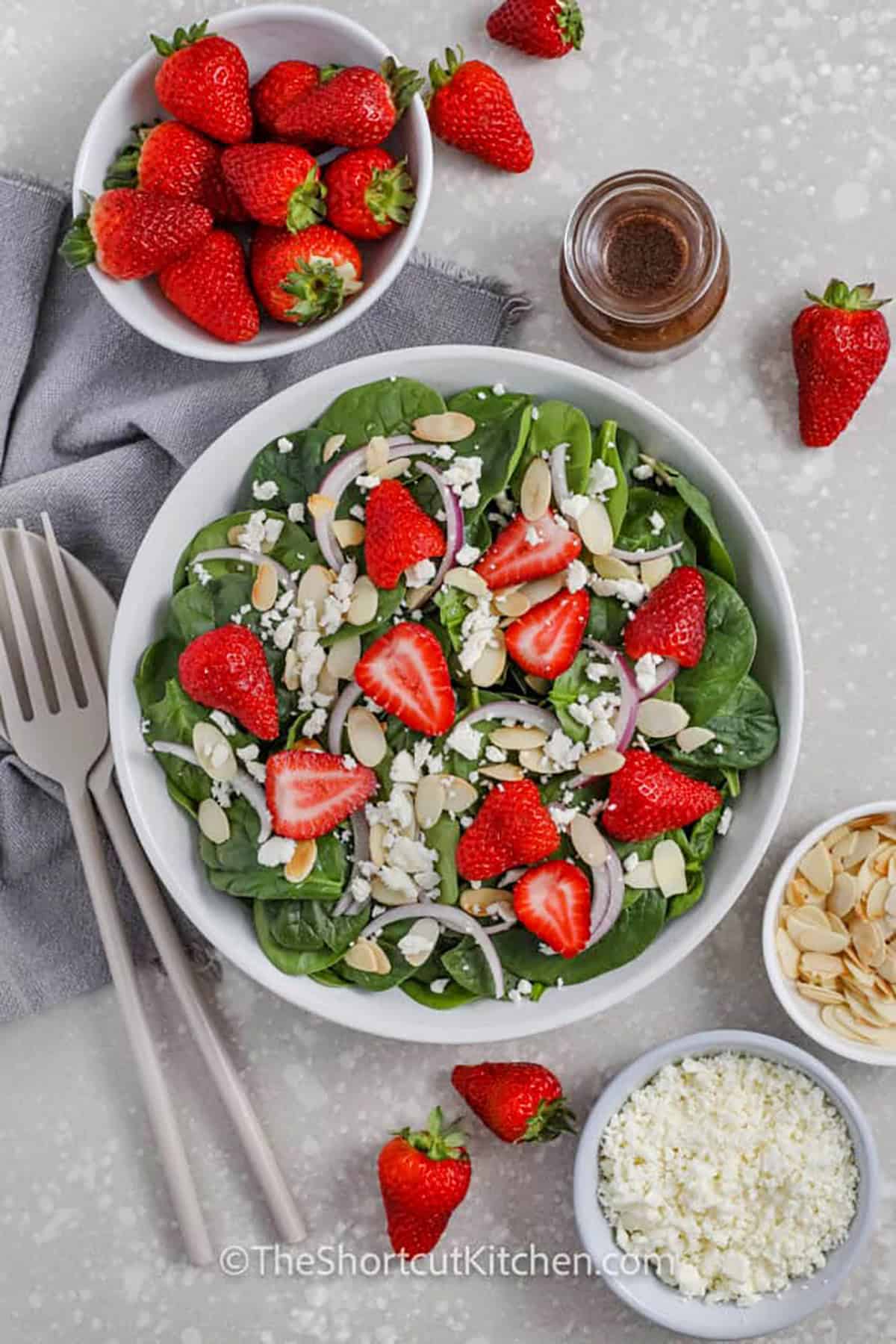 Brighten up any meal with a fresh and easy spinach and strawberry salad. This delicious recipe features tender spinach, sweet strawberries, crumbled feta, and sliced almonds. Toss it with a poppyseed or balsamic dressing for the best combination of flavors. Add extras like dried fruit, walnuts, or arugula for a twist. Whether for a quick lunch or a side dish, this salad is always a favorite! #theshortcutkitchen plated Spinach and Strawberry Salad with almonds onions and feta