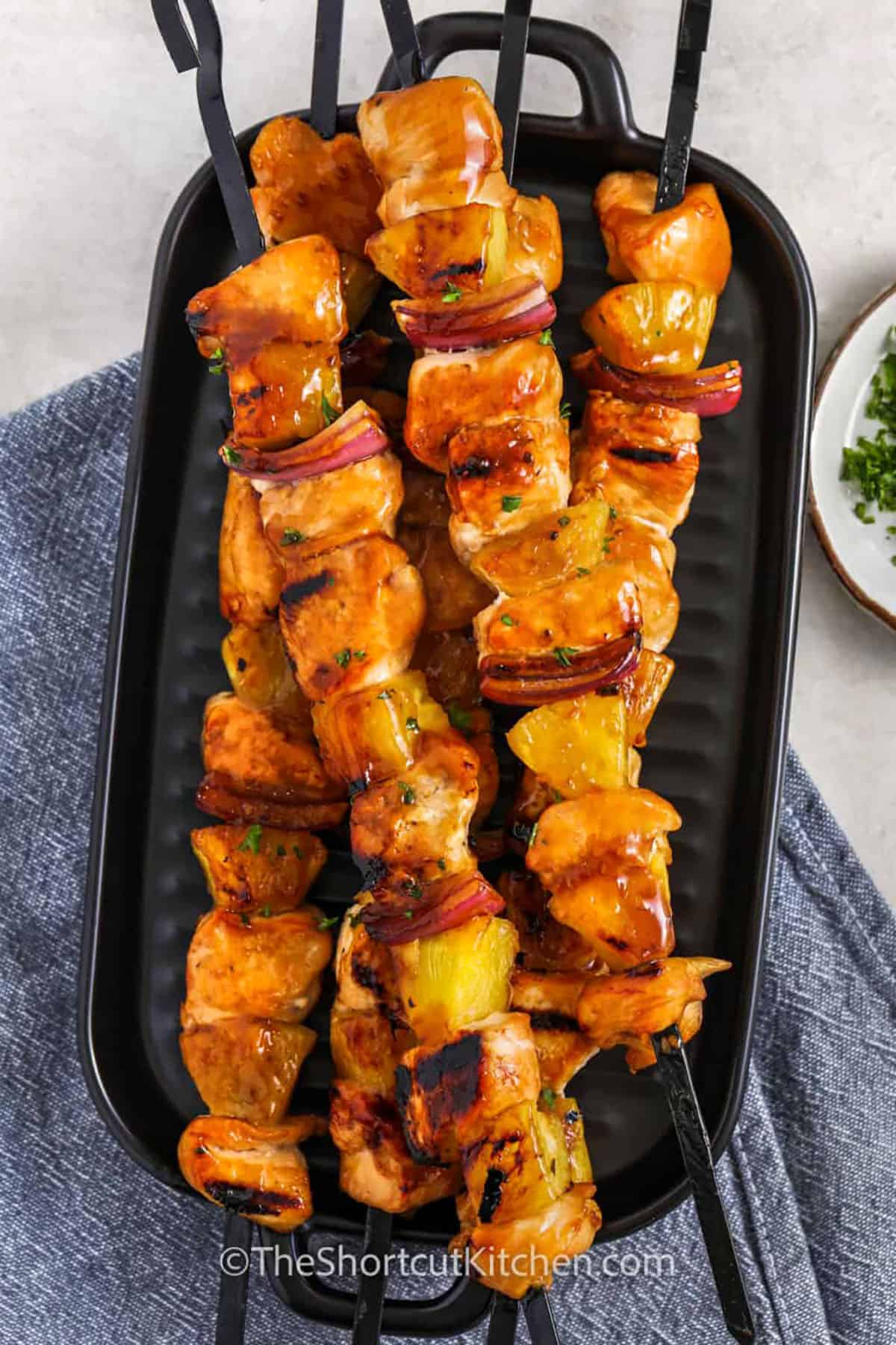 Chicken pineapple kabobs take just a few ingredients and turn them into something truly delicious! That teriyaki sauce adds so much flavor, and the pineapple gets that perfect little char on the grill. Add a squeeze of lime juice for a bright pop of flavor! These skewers are always a star on the dinner table. They taste just as good as they look on the plate! #theshortcutkitchen chicken pineapple kabobs on a serving dish