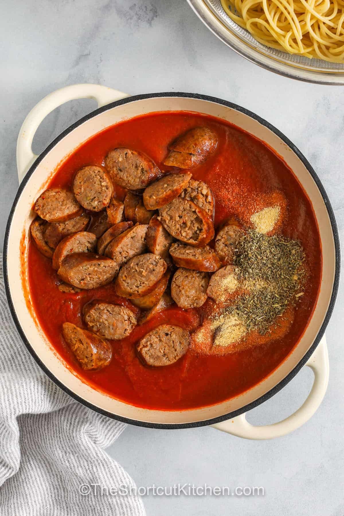 adding sausage and seasonings to pot with tomato sauce to make Italian Sausage Spaghetti