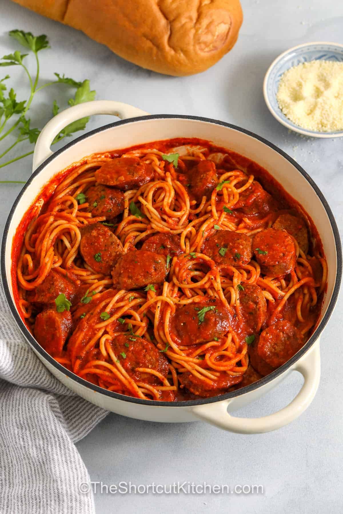 pot full of Italian Sausage Spaghetti with a loaf of bread and bowl of parmesan