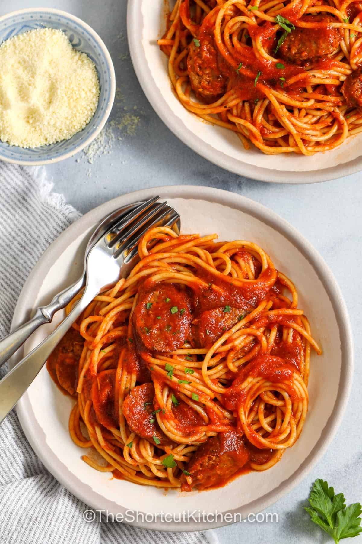 Italian sausage spaghetti is one of the best easy meals for a busy weeknight. Everything goes into one pot for a quick cleanup and a cozy, hearty dish. The sausage brings big flavor, and the marinara sauce ties it all together with just the right touch. This pasta recipe is simple but satisfying, making it a go-to for when dinner needs to be fast but full of taste. #theshortcutkitchen plated dishes of Italian Sausage Spaghetti with a bowl of parmesan