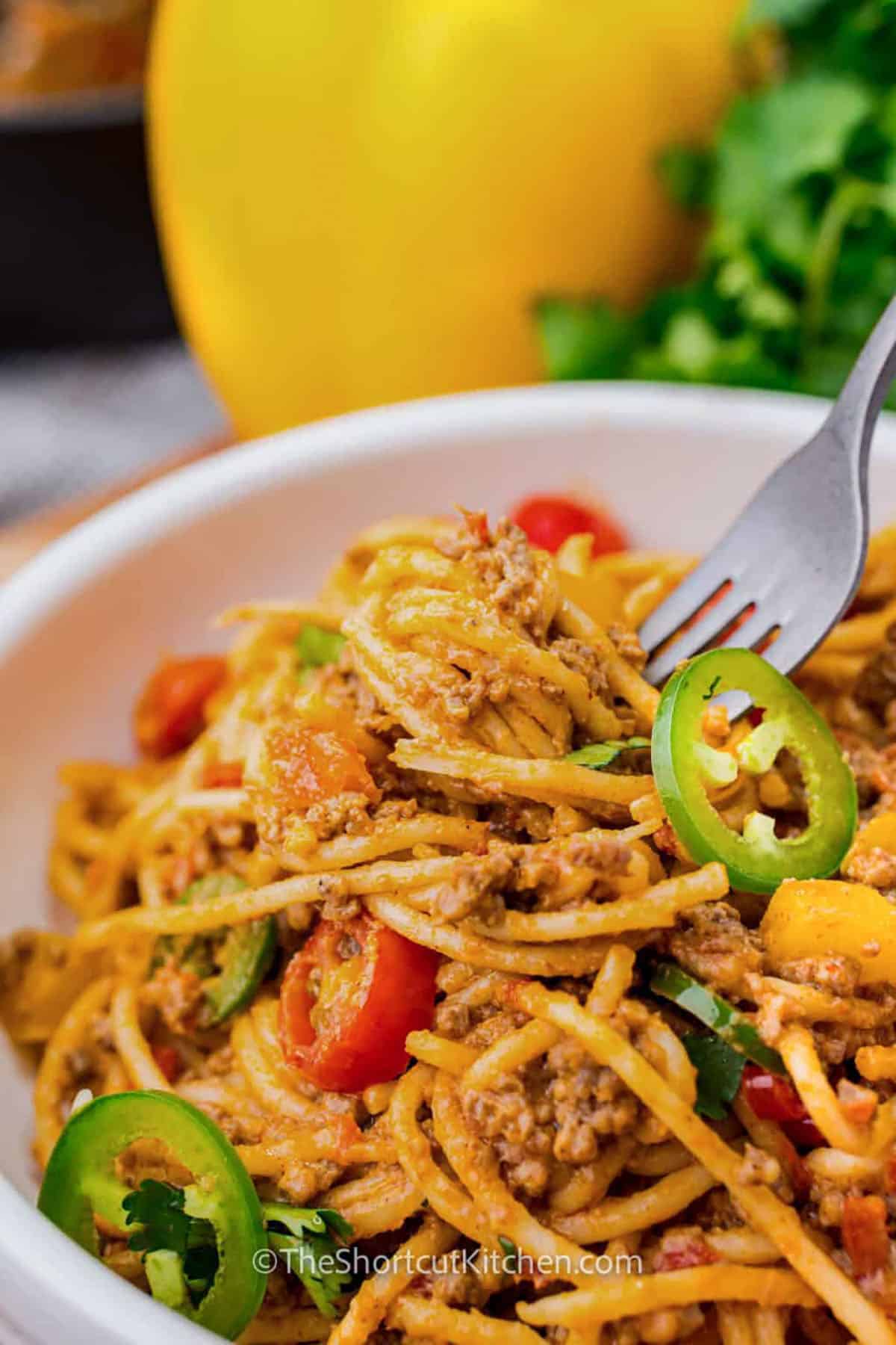 A taco spaghetti recipe is a cozy and cheesy twist on taco night that the whole family will love. Seasoned ground beef and peppers are mixed with spaghetti and a creamy, cheesy sauce. It all comes together in one pot, making cleanup easy. This recipe is a go-to for busy nights or anytime you need comfort food. Add your favorite Tex-Mex toppings to make it even better. #theshortcutkitchen plated Taco Spaghetti Recipe with a fork