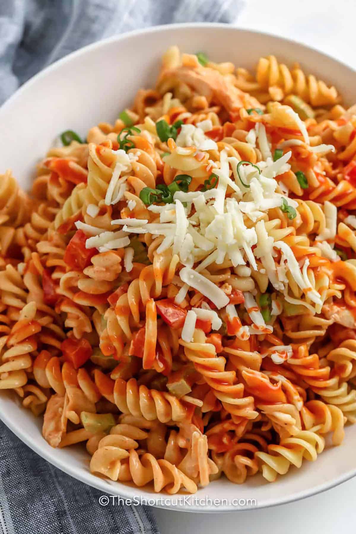 Buffalo chicken and pasta salad offers a spicy twist on traditional pasta salad with the addition of buffalo sauce and ranch dressing. Rotini pasta holds the dressing well, while shredded chicken provides hearty flavor and texture. This recipe is easy to customize by adding more veggies or adjusting the heat level to your taste. #theshortcutkitchen Buffalo Chicken and Pasta Salad with cheese