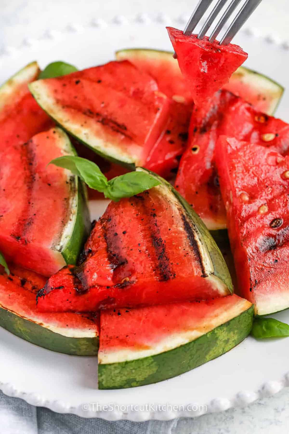 Grilled watermelon is a quick and easy dish that turns fresh melon into something truly special. Slices are brushed with tangy balsamic vinaigrette, then grilled until tender and marked with smoky char lines. The heat intensifies the sweetness and adds bold flavor, making this an unforgettable summer side. Serve it warm off the grill or chilled for contrast! #theshortcutkitchen Grilled Watermelon on a plate with a piece on a fork