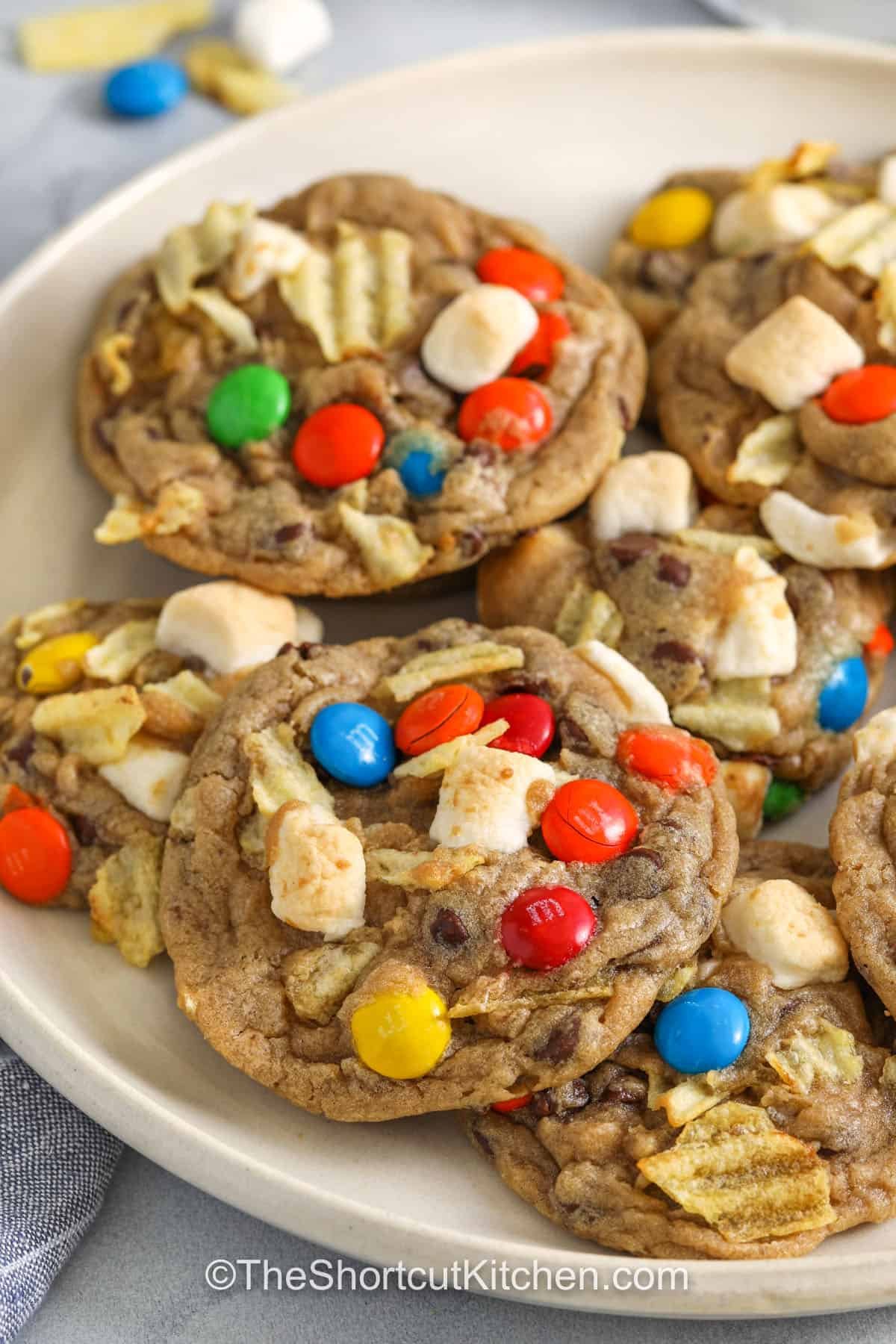 Kitchen sink cookies are a fun and tasty way to clear out your pantry and make something sweet! Add a mix of chocolate chips, nuts, dried fruit, even pretzels or toffee bits. They come out golden on the outside and soft in the center with the perfect chewy texture. They’re great for holidays or anytime treats! #theshortcutkitchen close up of plated Kitchen Sink Cookies