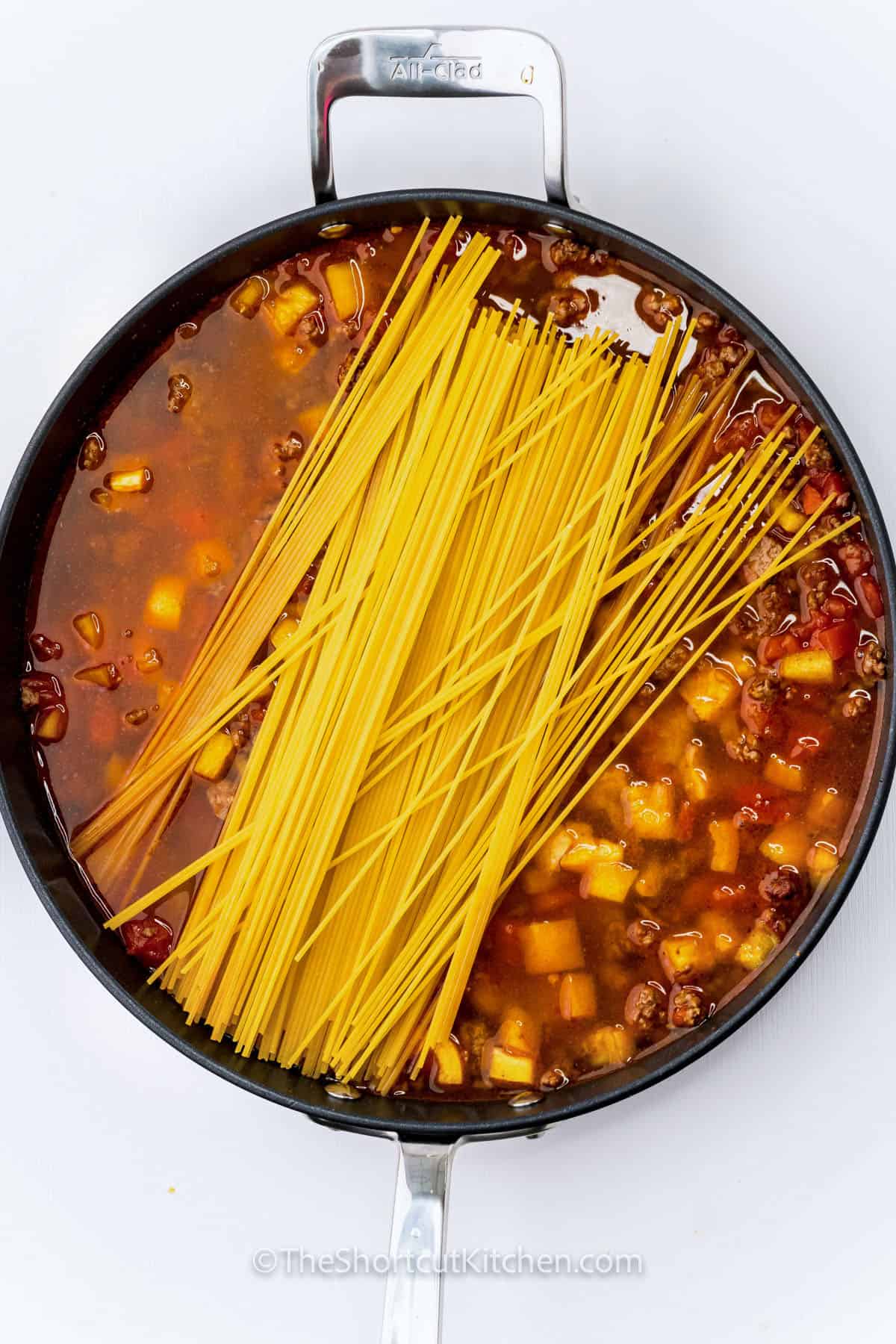 adding spaghetti to vegetables and meat to make Taco Spaghetti Recipe