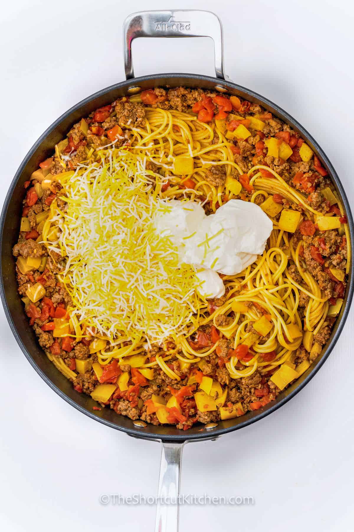 adding cheese and sour cream to spaghetti , meat and vegetables to make Taco Spaghetti Recipe