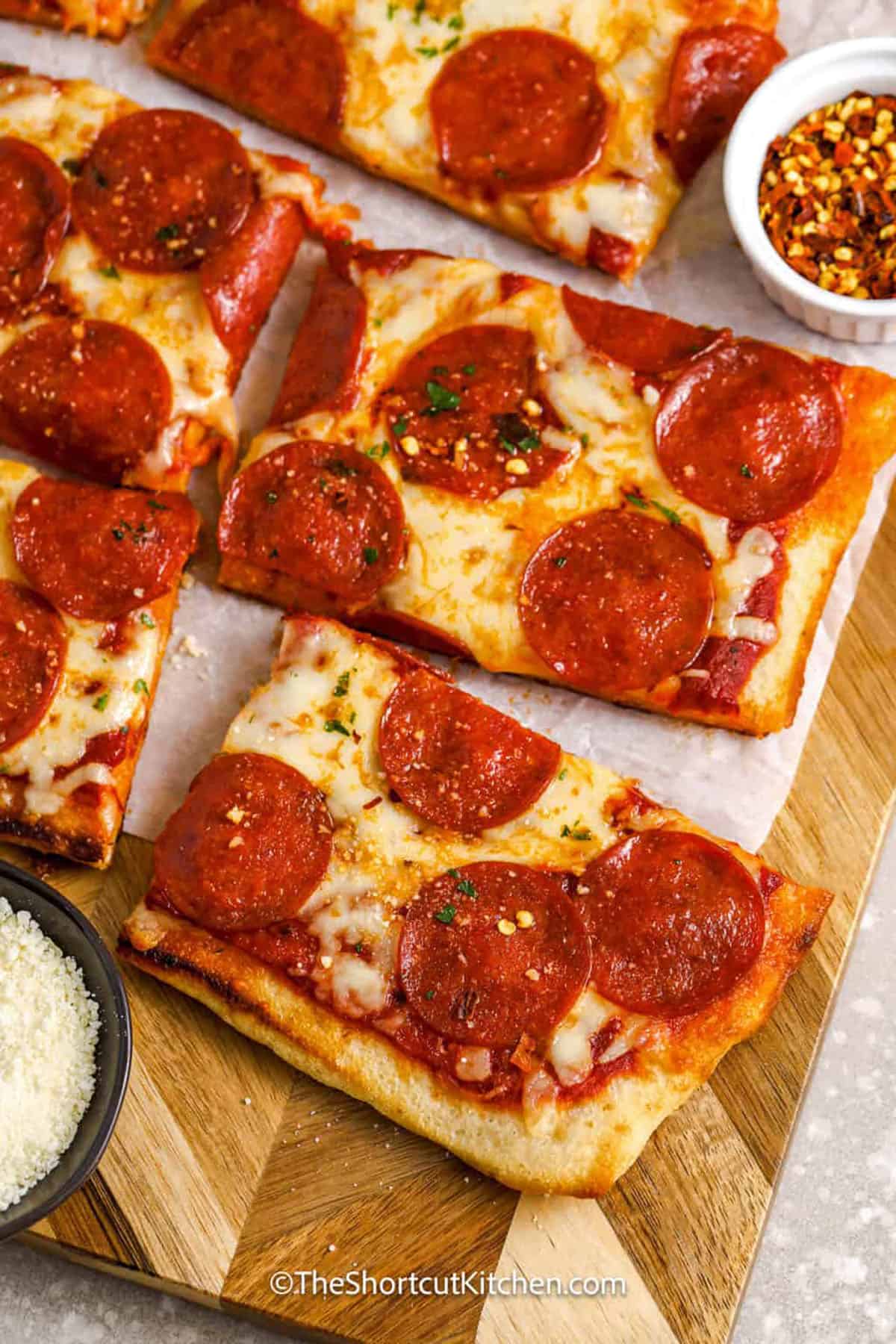 This shortcut grilled pizza recipe will give you and your guests the best crispy pizza with fresh homemade flavor. Start with refrigerated pizza dough and a jar of your favorite sauce from the store. Top with mozzarella and pepperoni and grill until melted and golden with a touch of flame-kissed char. Summer barbecue season just got even more fun with pizza night added to the mix. Set out an array of toppings and let the family make their own personal pizzas! #theshortcutkitchen close up of Grilled Pizza slices