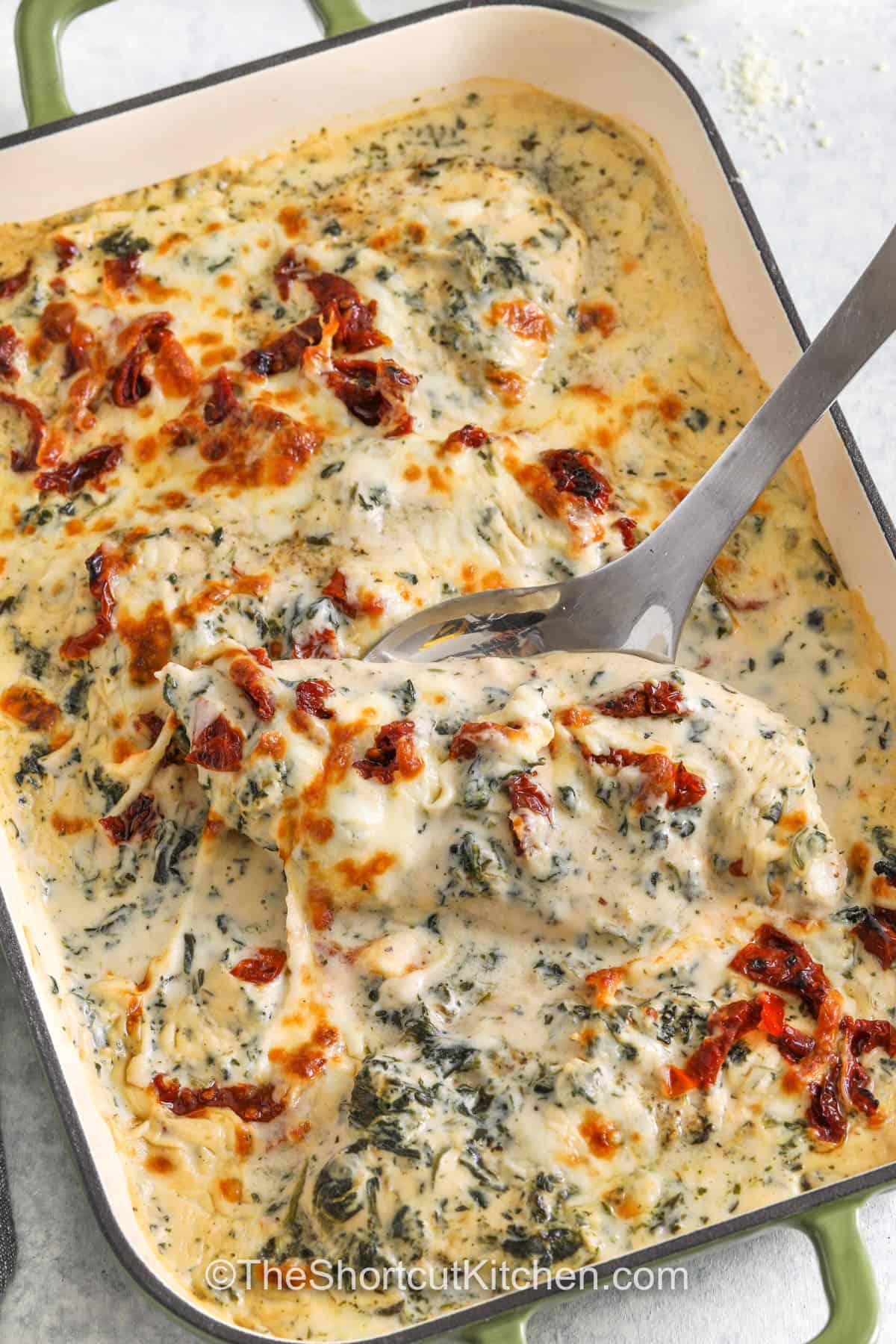 taking a piece of cheesy Baked Tuscan Chicken out of a dish