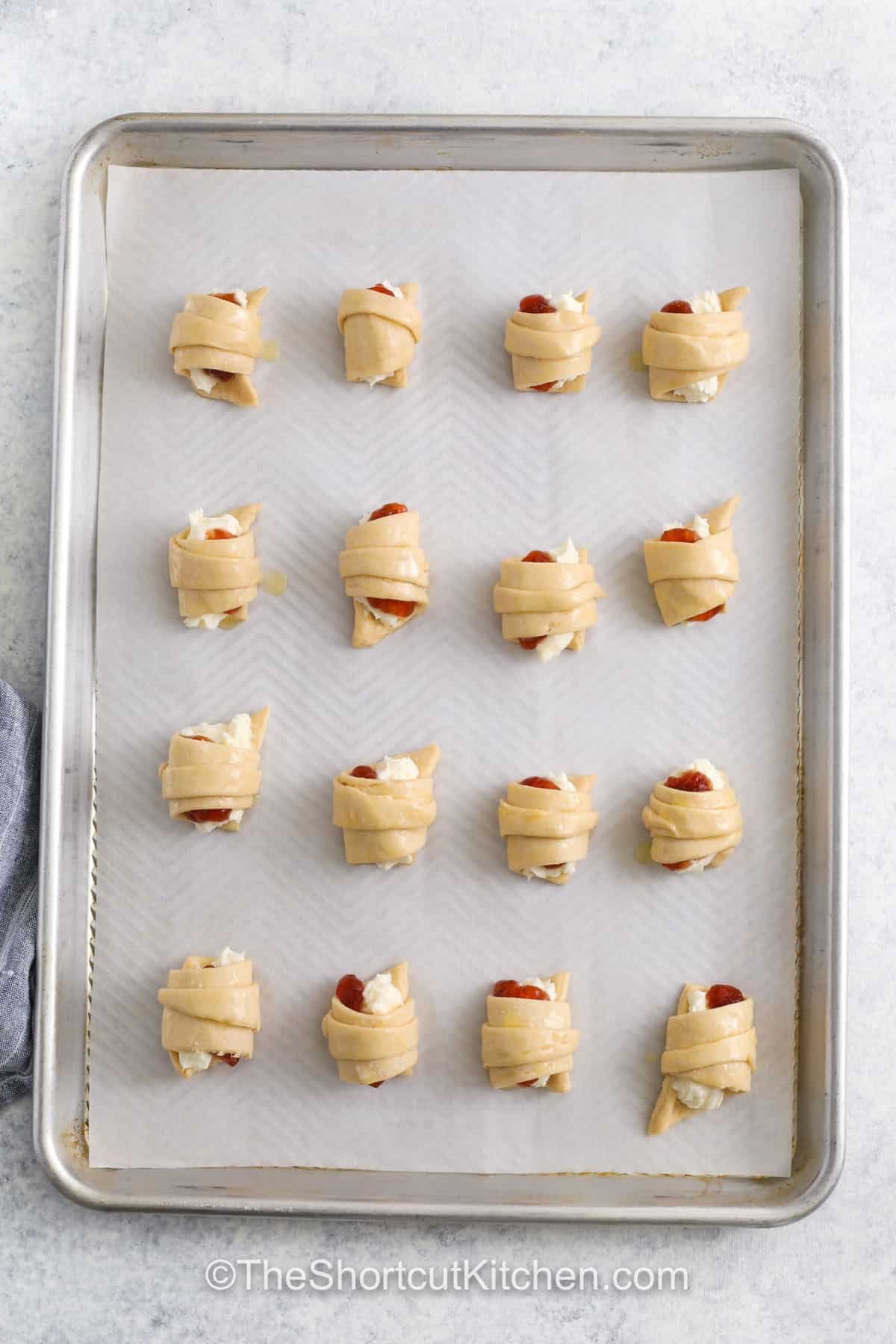 Cream cheese crescent rolls are a sweet and flaky pastry that’s perfect as a dessert or light breakfast. This easy recipe uses crescent roll dough wrapped around a filling of cream cheese and fruit jam or pie filling. Choose cherry, blueberry, or even apple. Brush with butter and bake, then sprinkle with cinnamon or add chocolate syrup for a fancy touch. These quick danishes are a favorite anytime treat! #theshortcutkitchen Cream Cheese Crescent Rolls on a sheet pan before cooking