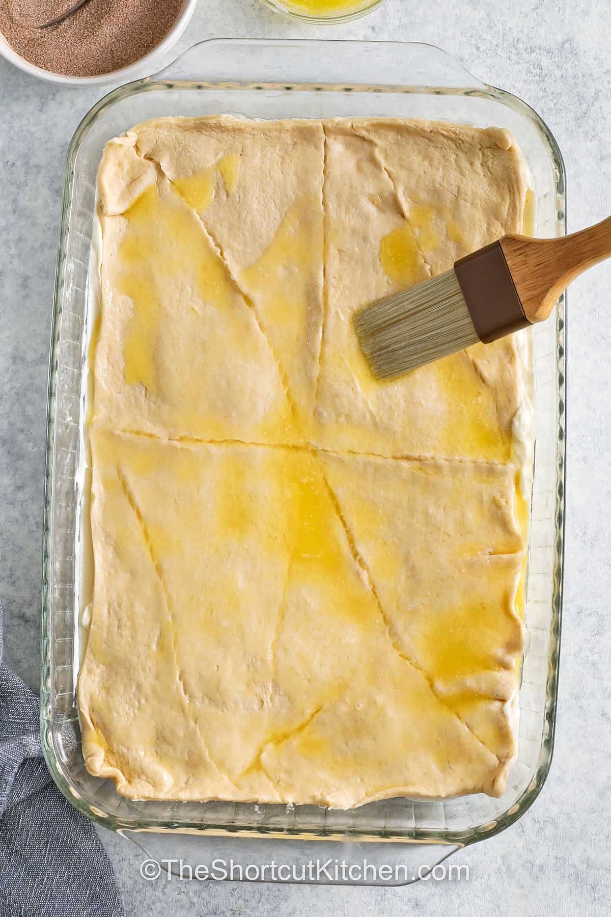 adding another layer of crescent roll dough to dish and brushing with melted butter