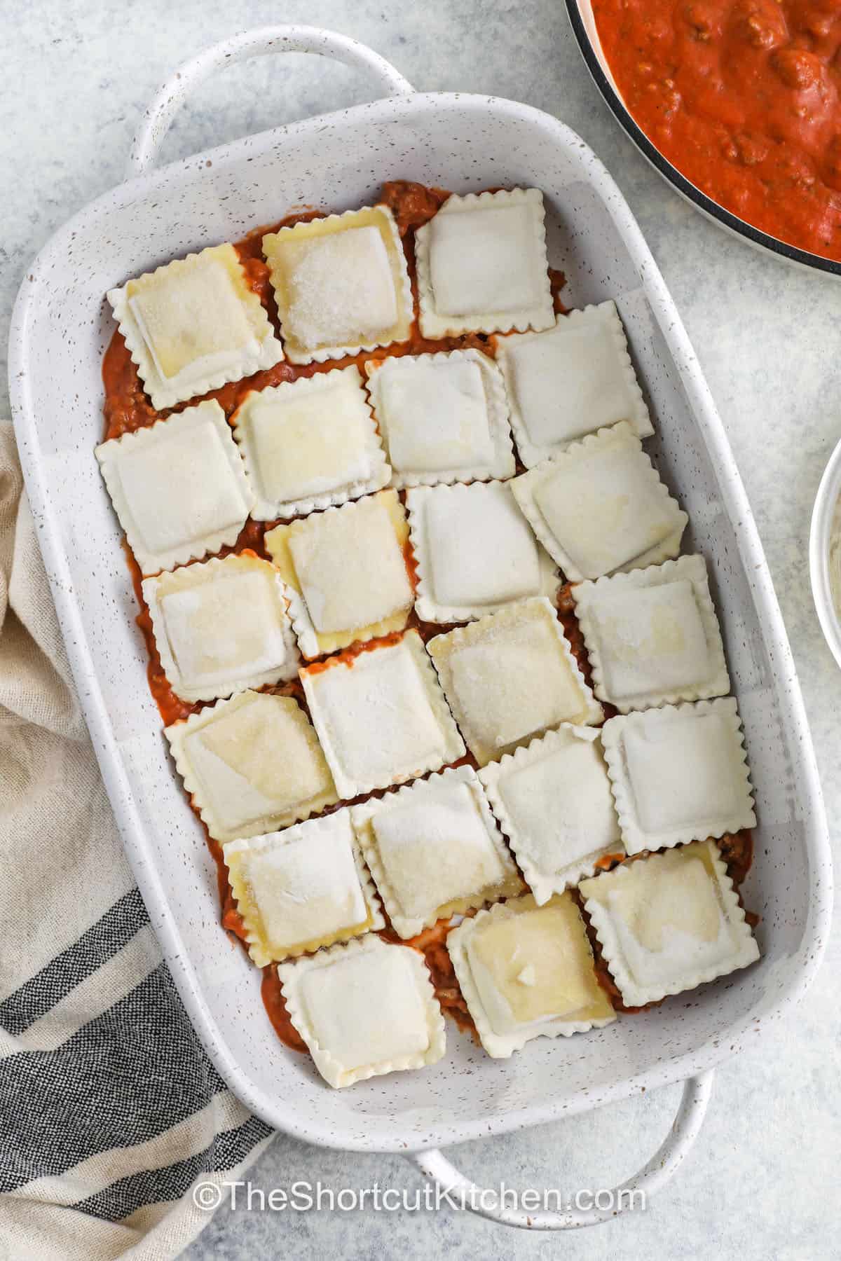 adding sauce and frozen ravioli to casserole dish to make Frozen Ravioli Bake