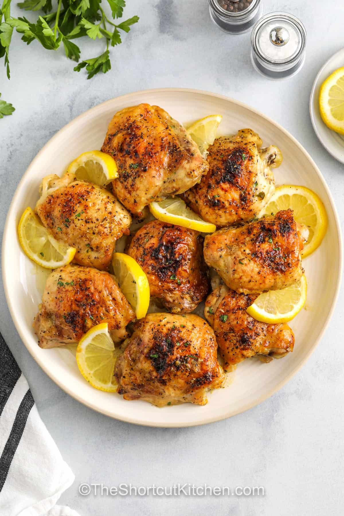 These lemon pepper chicken thighs are baked in the oven with a tangy citrus glaze and plenty of herbs for a savory twist. The skin turns perfectly crispy while the meat stays juicy and full of flavor. It’s an easy, one-pan dinner with that bright lemon pop in every bite. Quick to make and simple to serve with salad or bread. #theshortcutkitchen Lemon Pepper Chicken Thighs on a plate with lemon slices