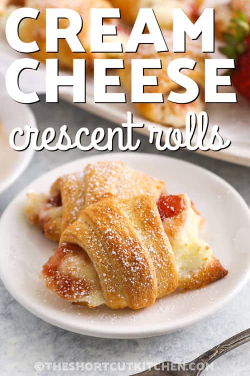 This cream cheese crescent rolls recipe with fruit filling is an easy method to make a sweet and creamy breakfast pastry. Crescent roll dough is rolled up around a filling of cream cheese and fruit jam or pie filling, then brushed with butter and baked until golden. Any fruit flavor can be used. Try cherry, blueberry, apple, or strawberry. Sprinkle with cinnamon, powdered sugar, or chocolate syrup and make it a dessert. This homemade danish will be a family favorite. #theshortcutkitchen plate of flaky Cream Cheese Crescent Rolls with writing