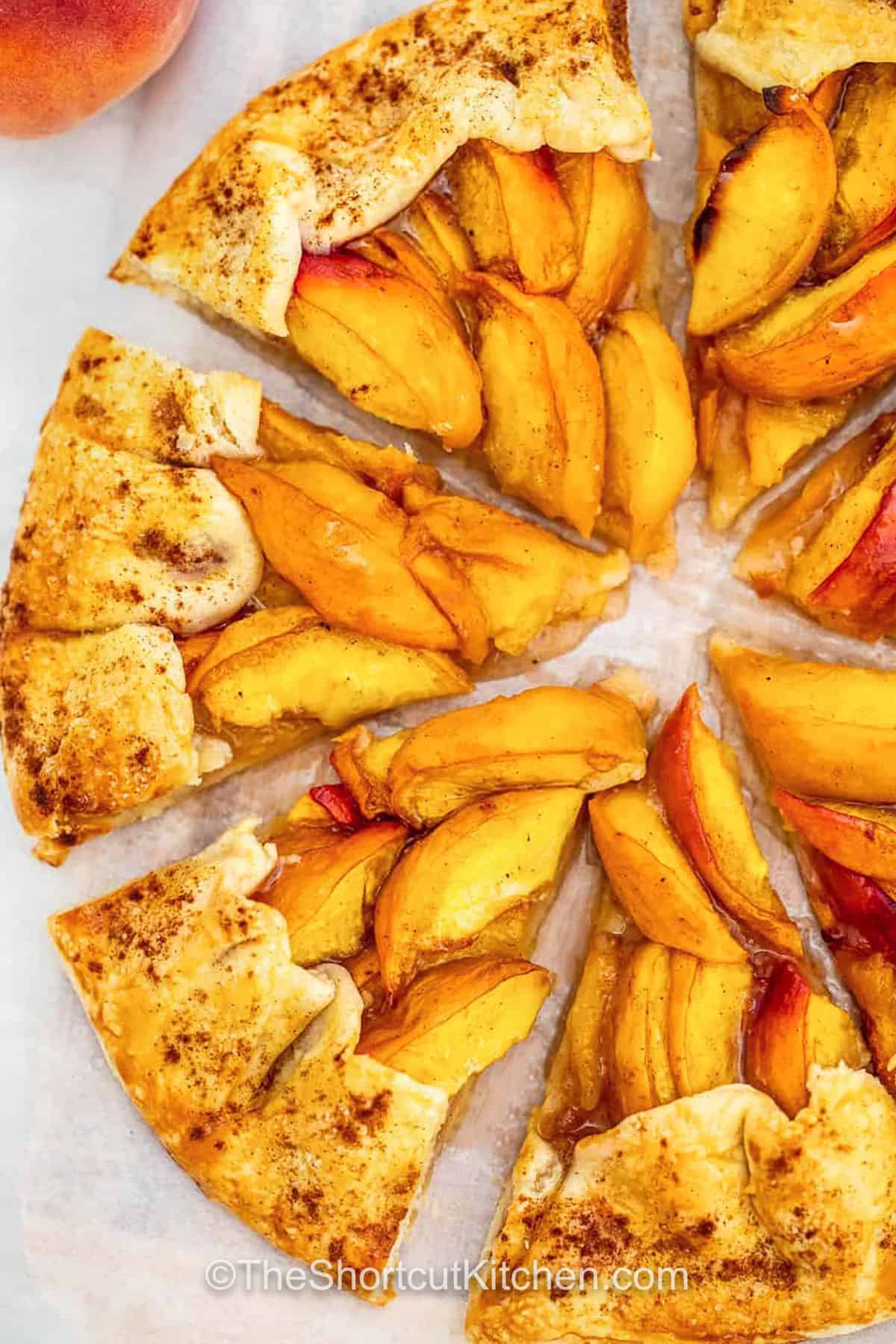 A peach galette recipe like this brings all the homemade goodness without the fuss. The fresh peaches are lightly sweetened and wrapped in a rustic, buttery crust that bakes up golden and crisp. It’s an easy open-face dessert that’s perfect for any summer get-together or even just a quiet evening treat. Every bite is sweet, tart, and warm with cozy flavor. This one is a keeper, you’ll want to pin and save. #theshortcutkitchen Peach Galette Recipe cut into slices