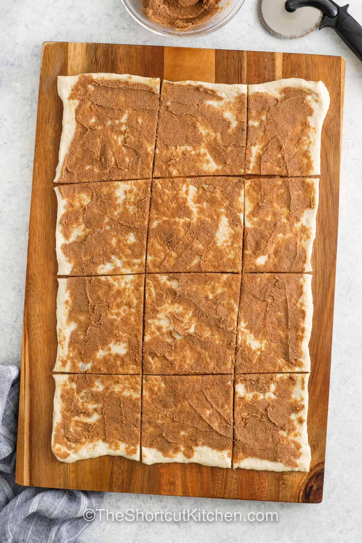 Treat your family to a sweet snack with this soft and fluffy cinnamon pull apart bread! Refrigerated pizza dough is the secret shortcut ingredient that makes this recipe quick and easy. The dough is spread generously with butter, brown sugar, and cinnamon, then sliced and stacked into easy pull-apart layers. After baking and drizzling with vanilla glaze, each bite delivers a burst of sweetness and cinnamon goodness. Try different versions with chocolate or pumpkin spice! #theshortcutkitchen adding brown sugar mixture to dough to make Cinnamon Pull Apart Bread