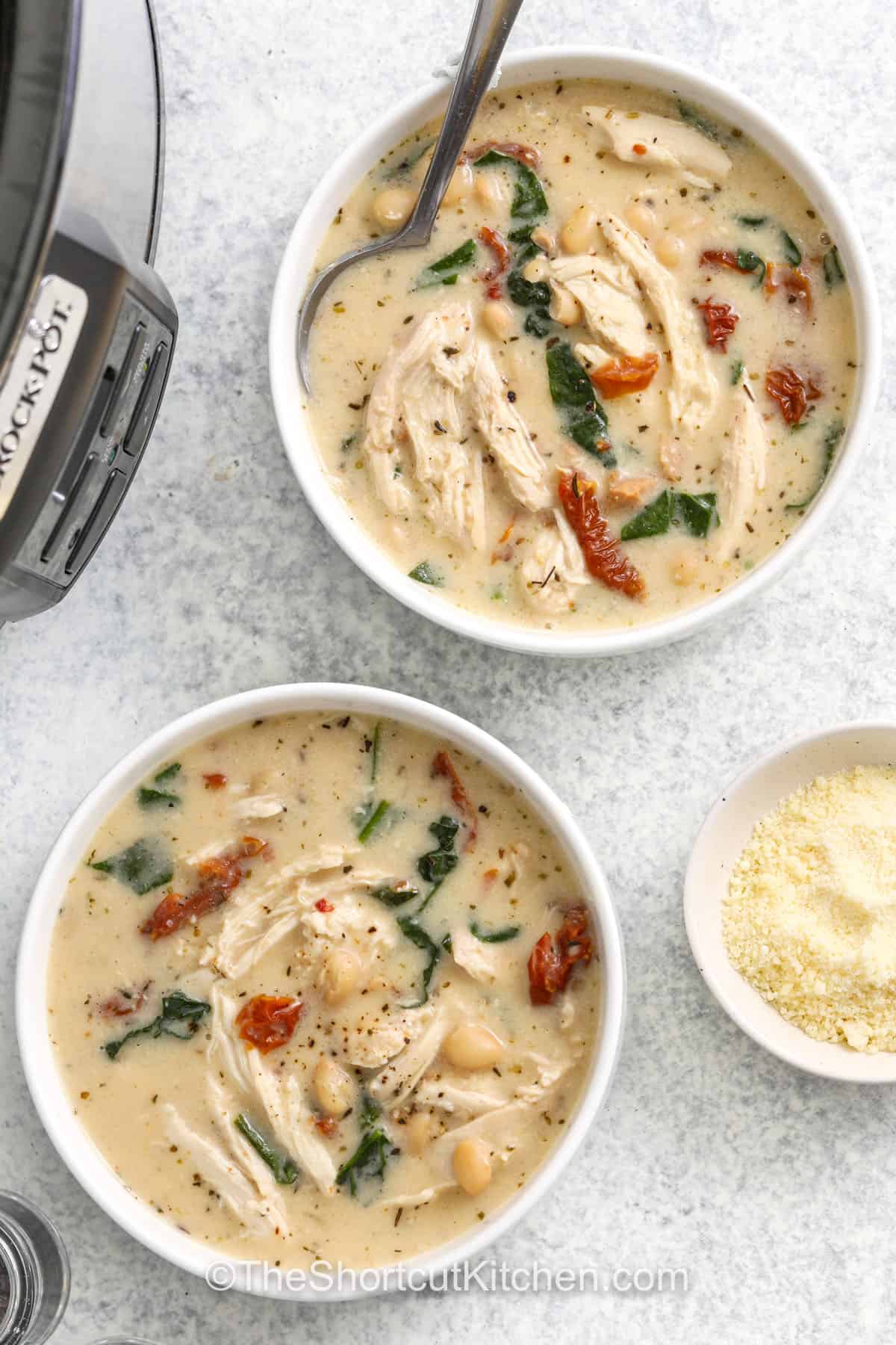 Tuscan chicken soup is a creamy, comforting blend of tender shredded chicken, white beans, and earthy spinach, all simmered together in a rich creamy broth. Sun-dried tomatoes and garlic bring deep flavor while Parmesan adds a savory finish. This delicious and easy slow cooker recipe is full of wholesome ingredients that come together for a bowl the whole family will love. #theshortcutkitchen top view of bowls of Crockpot Tuscan Chicken Soup