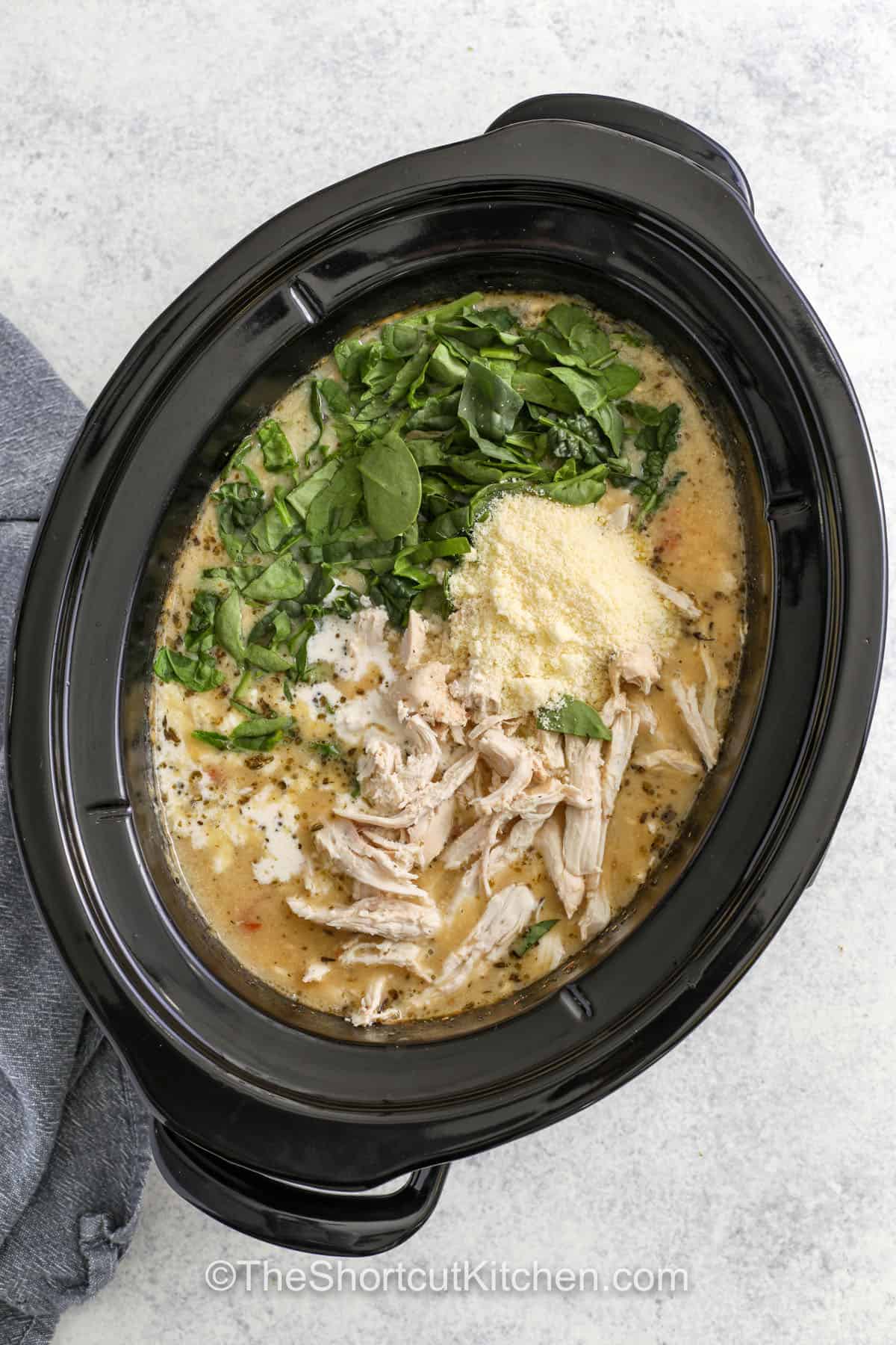 Tuscan chicken soup is filled with tender chicken, creamy broth, and white beans, all made in the slow cooker for easy prep. Spinach and sun-dried tomatoes give it color and flavor while Parmesan and garlic add a warm, savory finish. This simple recipe makes a hearty dinner that’s just right with a side of warm and crusty bread. #theshortcutkitchen ingredients in pot to make Crockpot Tuscan Chicken Soup