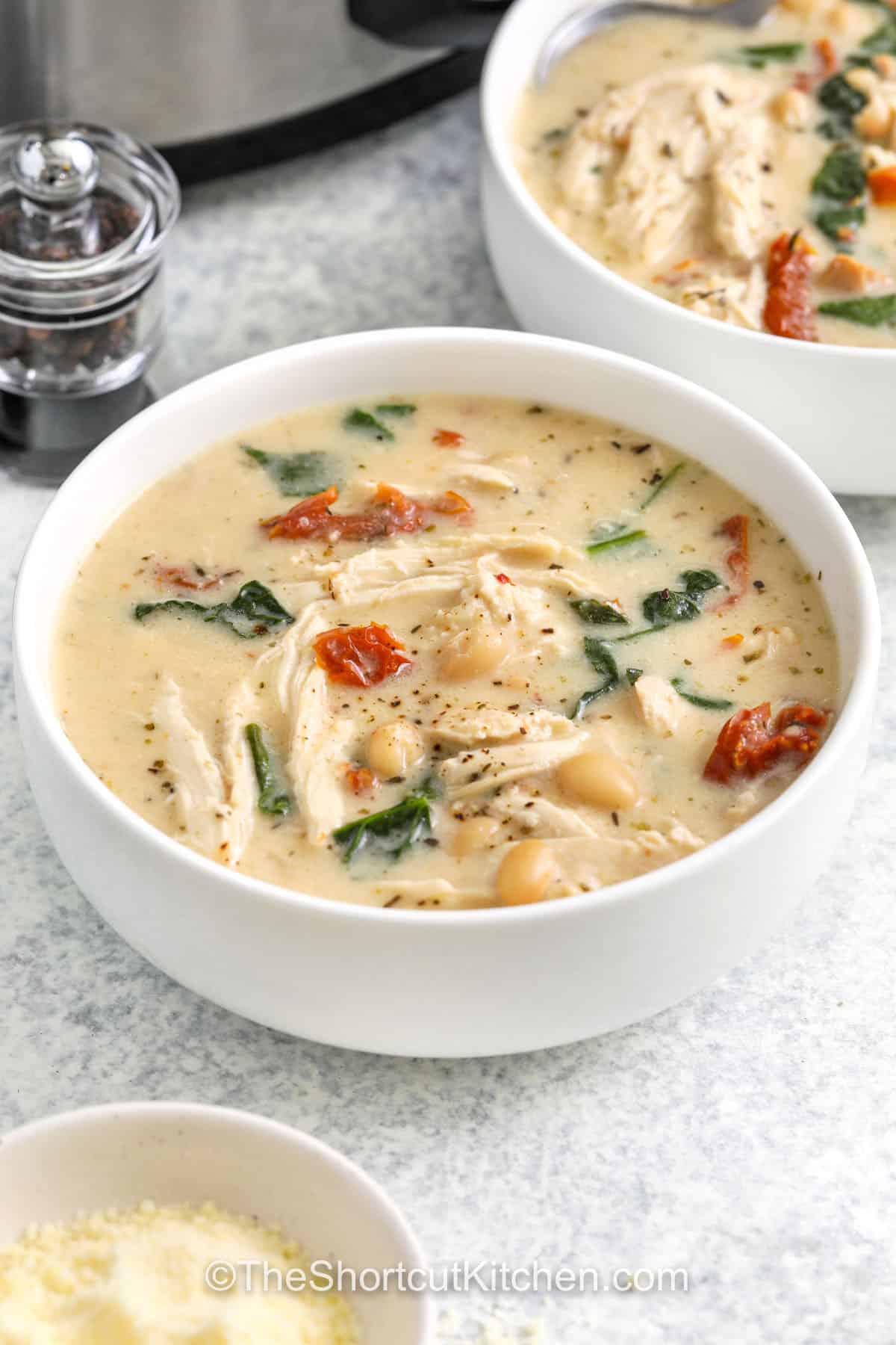 Tuscan chicken soup is full of rich, hearty flavors thanks to a creamy base, shredded chicken, white beans, and spinach. Sun dried tomatoes add a burst of savory goodness while garlic and Italian seasoning tie all the flavors together. Made in the slow cooker, this easy recipe is perfect for a cozy dinner that tastes like it came from a rustic Italian kitchen. #theshortcutkitchen close up of Crockpot Tuscan Chicken Soup in a bowl