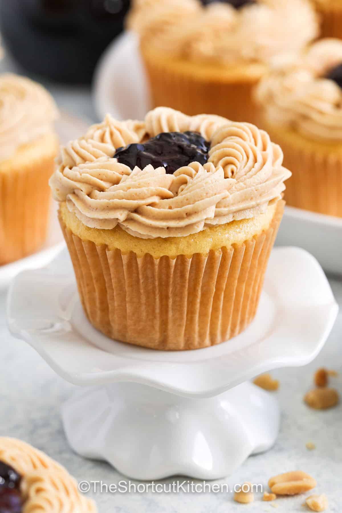 Peanut butter cupcakes combine the classic flavors of peanut butter and jelly in a fresh, fun way. The moist cake is soft and tender, making every bite melt in your mouth. Topped with a homemade peanut butter frosting that’s creamy and smooth, each cupcake gets a little surprise of grape jelly in the center, adding a burst of sweetness that’s just right. These cupcakes are a nostalgic treat reinvented for any occasion. #theshortcutkitchen Peanut Butter Cupcakes with grape jelly with peanut butter frosting