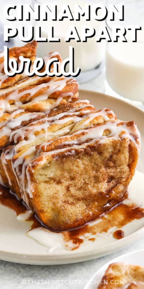 Who doesn’t love the irresistible taste and aroma of cinnamon pull apart bread! This recipe is so simple, made with refrigerated pizza dough from a can. Just roll out the dough and spread with butter, brown sugar, and cinnamon. Then cut into rectangles and stack them sideways in a bread pan. Bake until fluffy and golden, and drizzle with a simple glaze. Each layer easily pulls apart into melt-in-your-mouth goodness. It’s the best thing since monkey bread! #theshortcutkitchen plated Cinnamon Pull Apart Bread with glasses of milk and writing