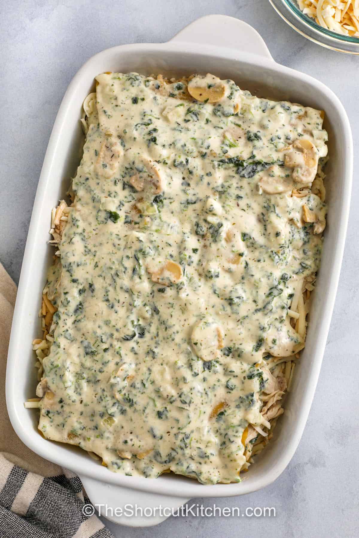 adding sauce on top of lasagna to make Chicken Alfredo Lasagna Recipe