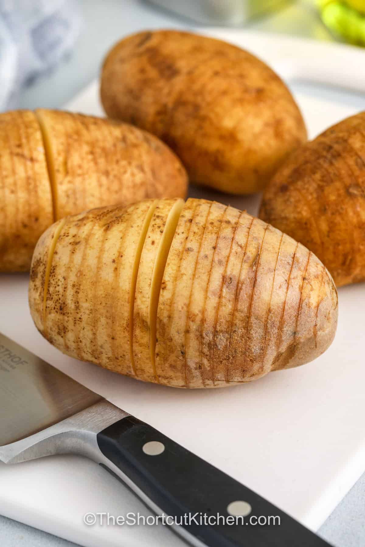 This easy Hasselback potatoes recipe turns a plain potato into the best crispy side dish for dinner. The potatoes are sliced thin, brushed with garlic butter, and baked in the oven until golden brown. Add bacon and cheese between the layers for a melty, smoky twist that feels perfect for a holiday meal. This dish is simple, elegant, and always a crowd-pleaser. #theshortcutkitchen. slicing potatoes to make Hasselback Potatoes Recipe