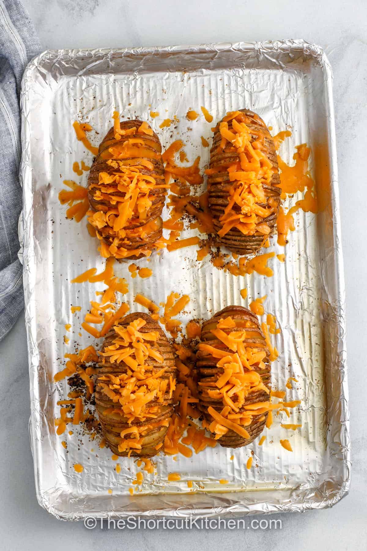 This Hasselback potatoes recipe is easy, cheesy, and always a holiday favorite. Potatoes are carefully sliced, brushed with garlic butter, and baked in the oven until the tops are crispy. The layers hold melty cheese that makes every bite delicious. Serve them as the best side for dinner or dress them up with toppings to enjoy as a stand-alone dish. #theshortcutkitchen. adding cheese to potatoes to make Hasselback Potatoes Recipe