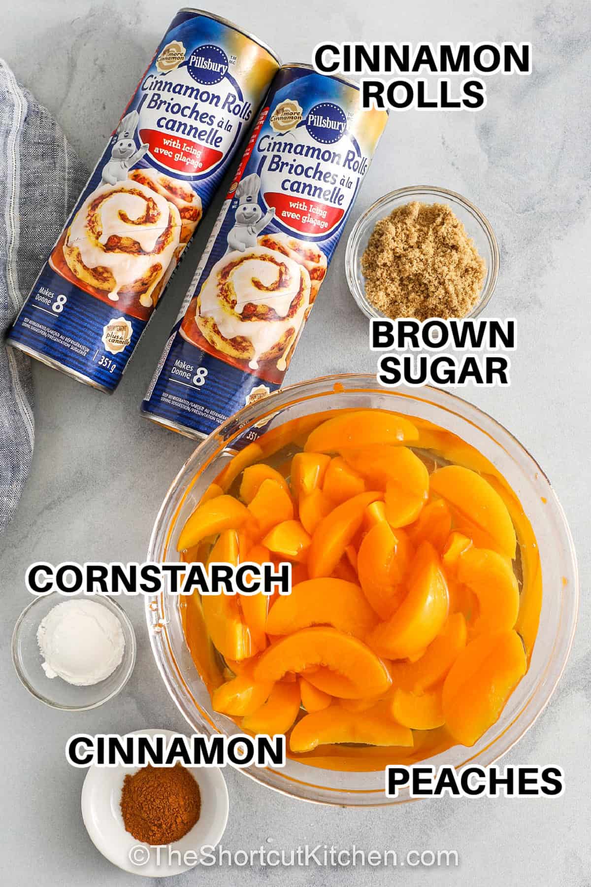 Cinnamon roll peach cobbler brings together easy ingredients for a homemade-tasting dessert. Canned peaches are topped with cinnamon rolls and baked until golden, creating a quick and simple recipe full of flavor. This warm and bubbly cobbler is perfect for summer parties, potlucks, or a weeknight treat. No matter the occasion, everyone will love how cozy and delicious it tastes. #theshortcutkitchen cinnamon rolls , brown sugar , cinnamon , cornstarch, peaches with labels to make Cinnamon Roll Peach Cobbler