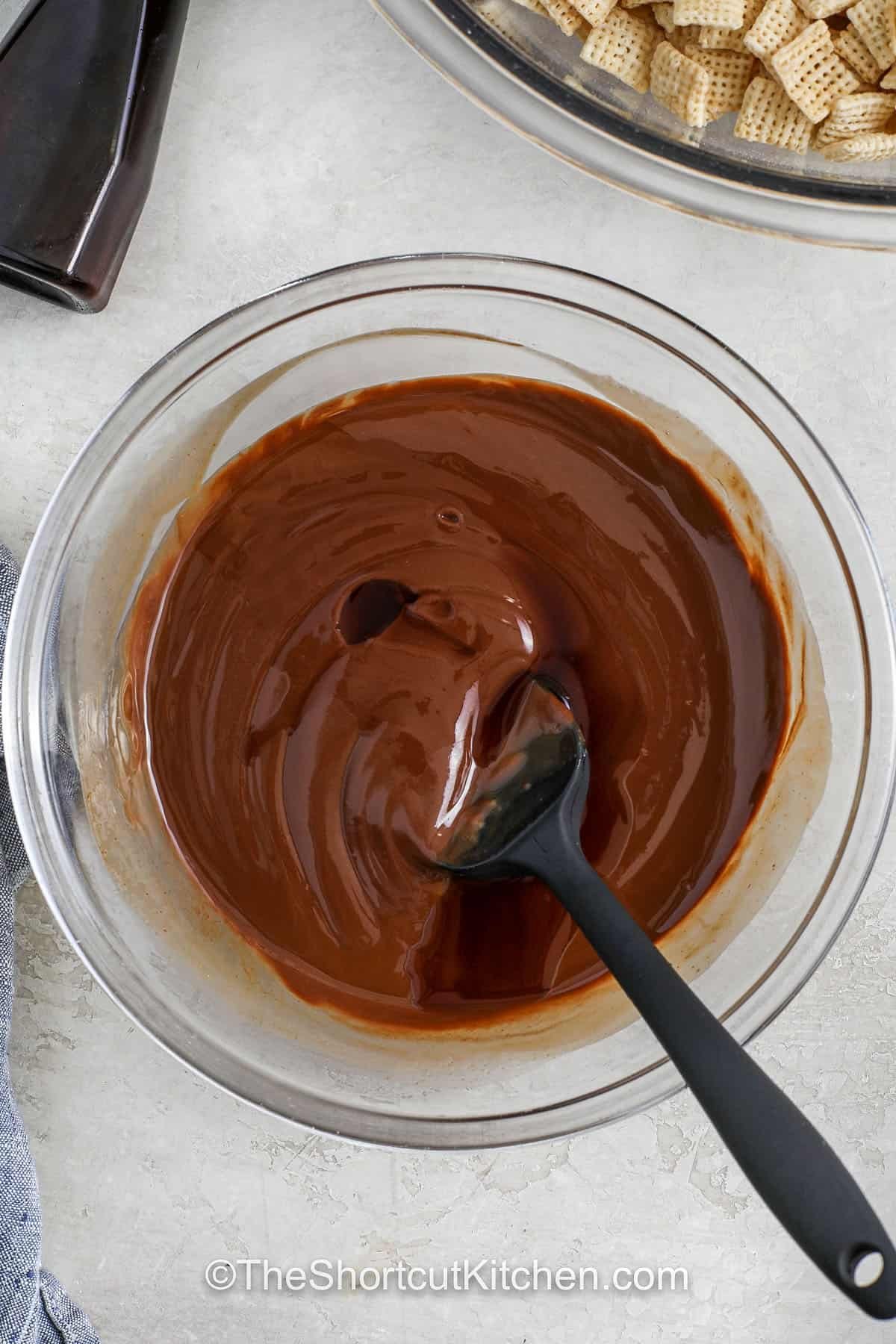 Muddy buddies lovers know the secret is in the coating. Melted chocolate, butter, and peanut butter make the cereal extra rich, and vanilla adds depth. Toss it all with powdered sugar for a light, sweet finish. It’s ideal for road trips, holiday snacks, or after-school treats. Make a big batch and store it in the fridge for a chilled twist that keeps it fresh longer and extra crunchy. #theshortcutkitchen a bowl of melted chocolate, peanut butter and butter