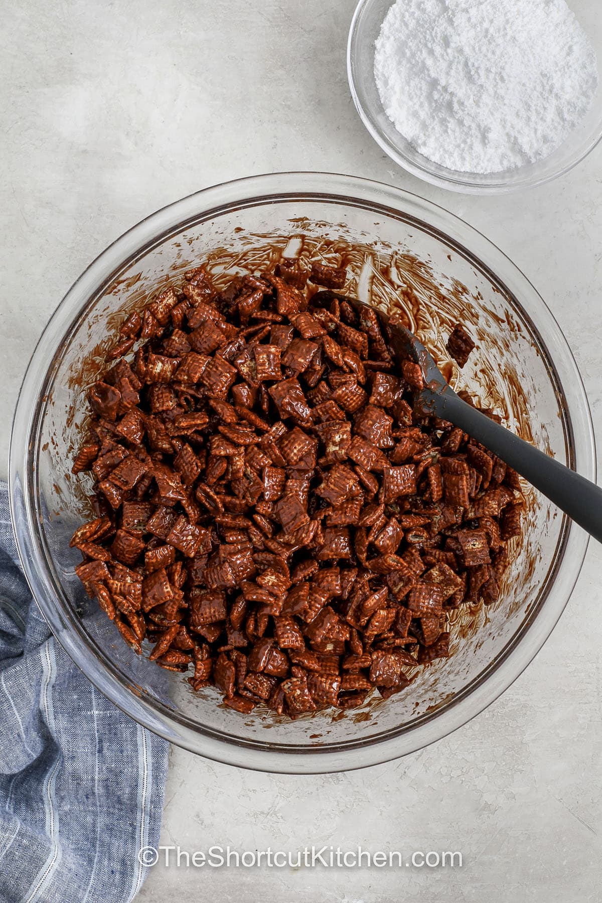 This Muddy Buddies recipe makes the perfect combo of salty, sweet, crunchy, and soft. Use corn, rice, or wheat Chex, depending on your texture preference, and customize it with extras like candy pieces or nuts. The base recipe is quick, reliable, and full of flavor. Great for gifting, lunchboxes, or late-night snacking. Plus, cleanup is easy, just one bowl, one bag, and you’re done in under 15 minutes. #theshortcutkitchen the chocolate mixture being combined with chex cereal in a bowl