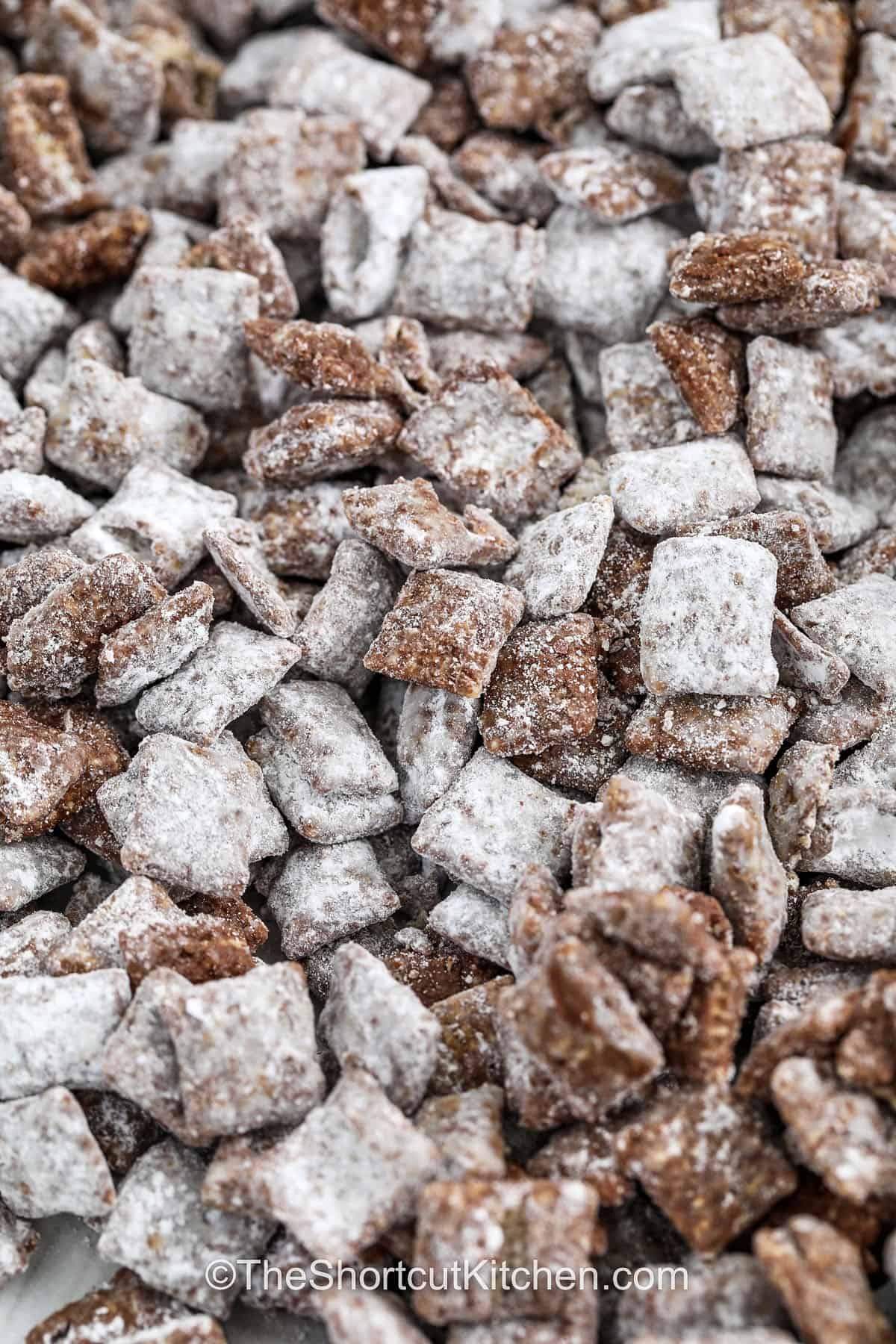 A muddy buddies recipe like this one is your ticket to stress-free snack prep. With no stove or oven needed, just microwave, mix, and shake for a dangerously delicious treat. Keep it classic with semisweet chocolate or try dark for a richer flavor. It's endlessly customizable and always a favorite at school events, office parties, and game days. Store in an airtight container for snacking all week. #theshortcutkitchen muddy buddies prepared on a baking sheet