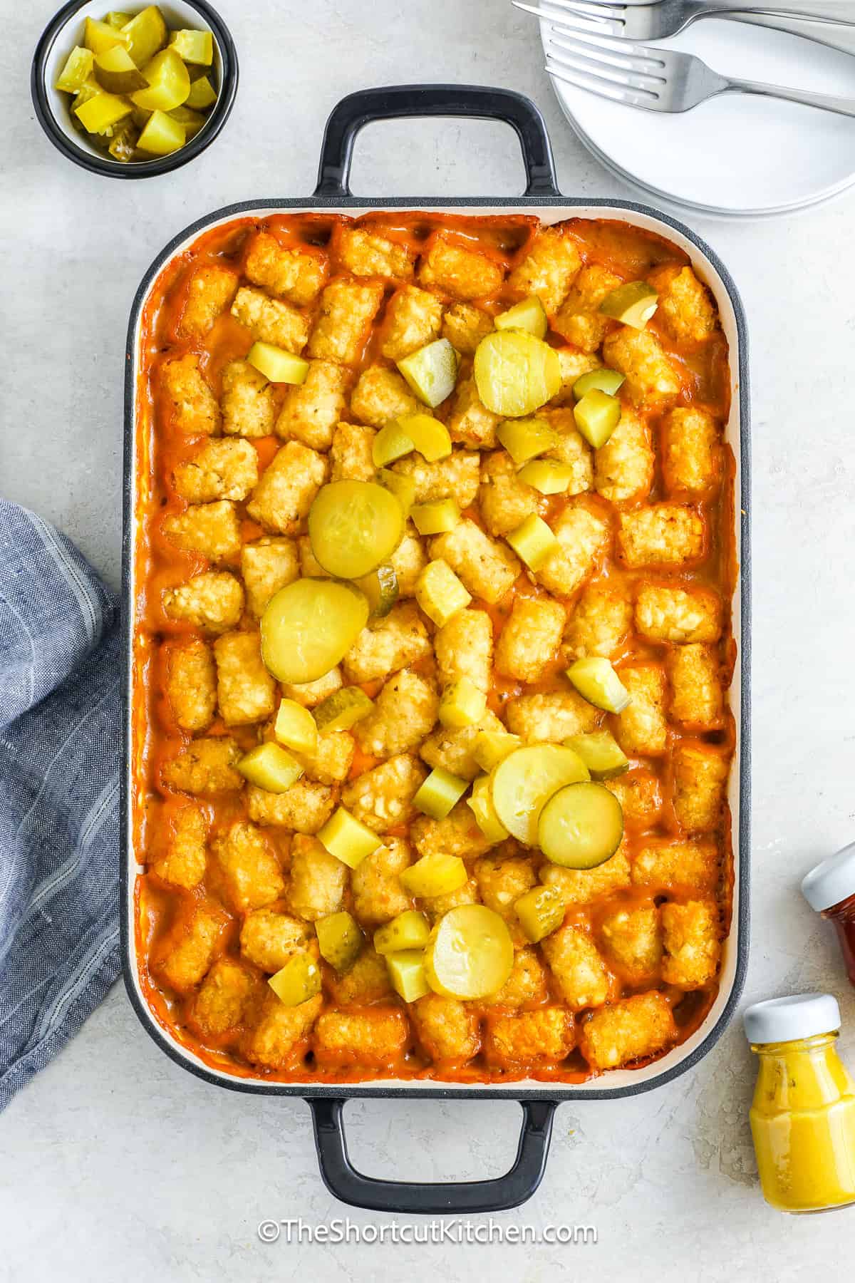 This cheeseburger tater tot casserole turns a classic comfort food craving into a golden, cheesy feast. Juicy ground beef and onions are combined with creamy cheddar soup, shredded cheddar, tangy mustard, and barbecue sauce, then baked under a blanket of crispy tater tots. Finish with chopped pickles if desired for a true burger twist. It’s fun to make, fun to eat, and perfect for any holiday, game day, or cozy dinner night. #theshortcutkitchen Baked cheeseburger tater tot casserole topped with sliced pickles