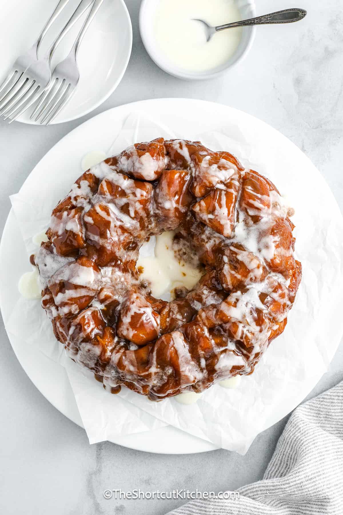Cinnamon roll monkey bread is the best kind of shortcut, quick, indulgent, and unbelievably easy. Start with refrigerated rolls, coat them in a buttery brown sugar and cream sauce, then bake until golden and gooey. Once inverted and glazed, you’ve got a sweet, sticky, pull-apart treat that’s perfect for breakfast, brunch, or any holiday occasion. You won’t believe what you can make with just a few simple ingredients. #theshortcutkitchen Cinnamon Roll Monkey Bread on a serving plate drizzled with icing