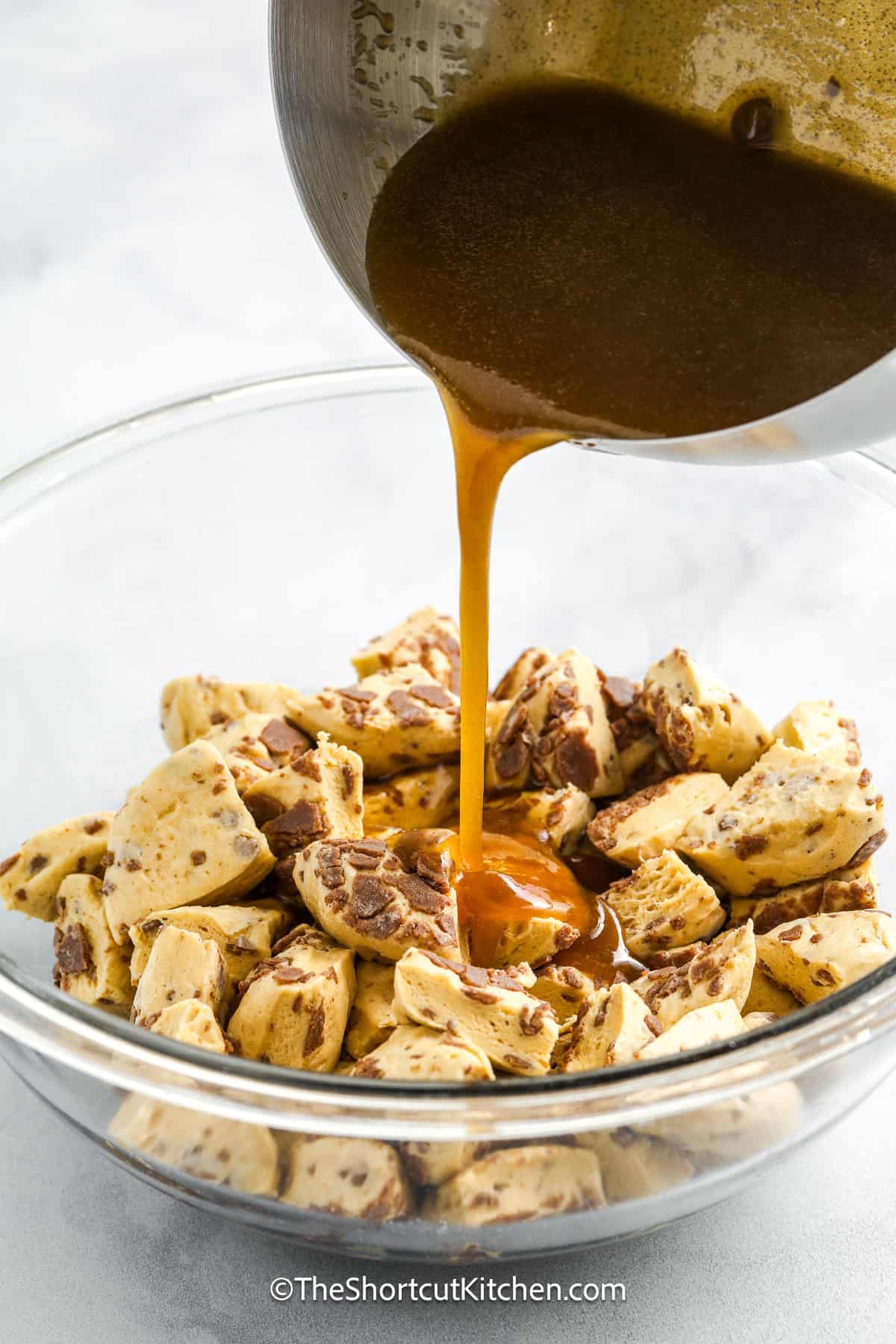 Cinnamon roll monkey bread is the ultimate shortcut recipe made with refrigerated rolls and a rich caramel cream sauce. Each bite is soft, gooey, and sweet, with a hint of cinnamon. This easy, pull-apart dessert is topped with icing for a perfectly glazed finish. It’s the best treat to make for breakfast, brunch, or a last-minute holiday gathering. You’ll be amazed at what you can do with so little effort. #theshortcutkitchen monkey bread sauce being poured over chopped refrigerated cinnamon rolls