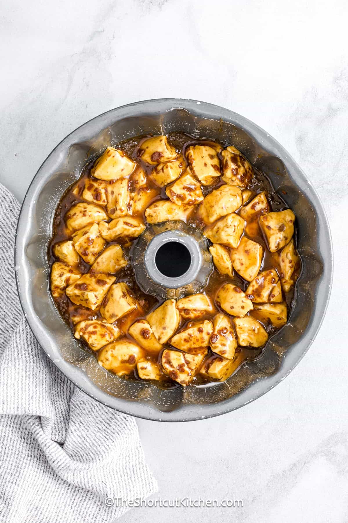Cinnamon roll monkey bread is a deliciously sticky, gooey treat that’s shockingly easy to make. Start with canned cinnamon rolls, toss with butter, brown sugar, and cream, then bake to perfection in a bundt pan. The final touch is a sweet glazed icing drizzle. Great for brunch, a quick dessert, or your next holiday gathering. This shortcut recipe is one of the best things you can pull off without breaking a sweat! #theshortcutkitchen monkey bread prepared in a a bundt pan