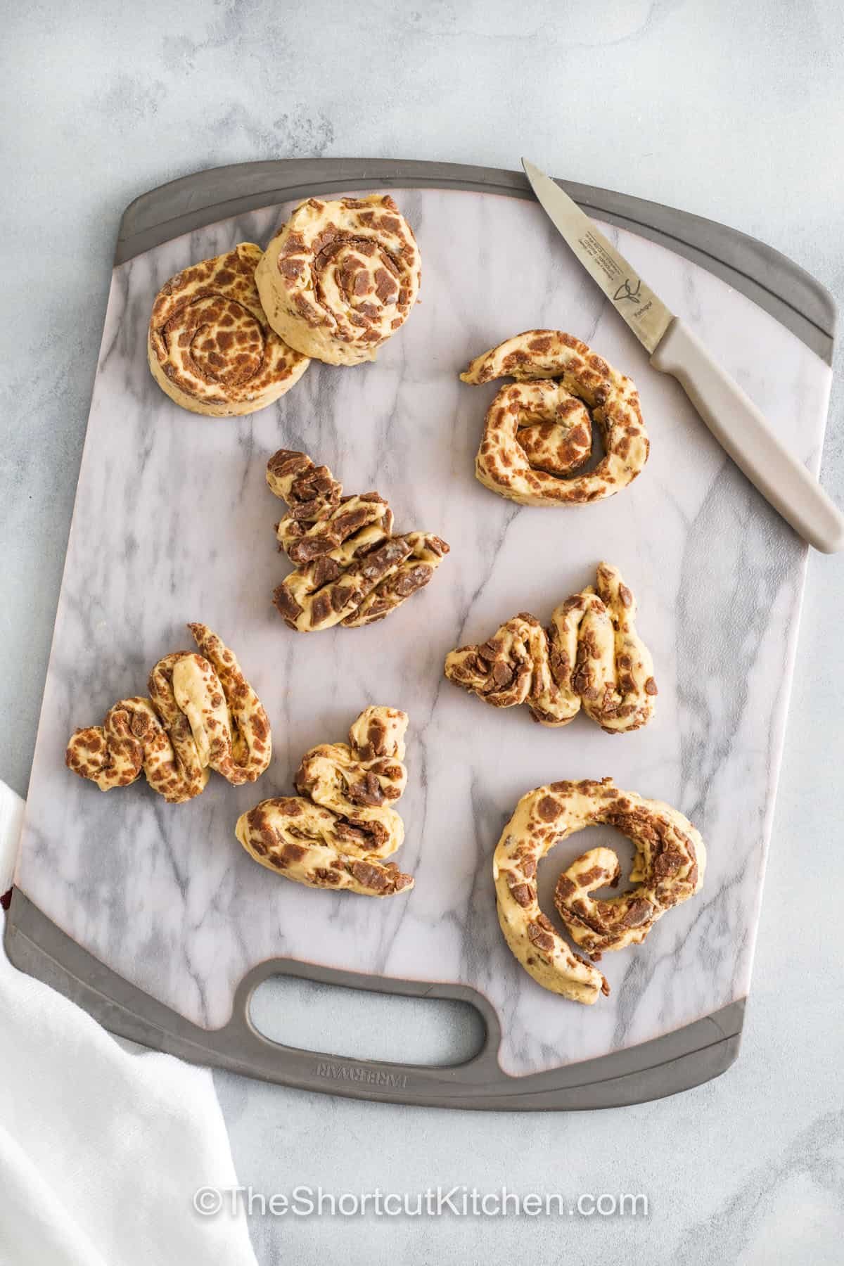 Cinnamon roll Christmas tree pastries are a festive, kid-friendly treat that’s easy to make at home. Soft and fluffy with warm cinnamon flavor, each roll is shaped like a tree and topped with sweet icing and colorful sprinkles. Perfect for holiday breakfasts, brunches, or dessert tables, these playful treats are quick to bake and guaranteed to delight everyone at the table. #theshortcutkitchen shaping cinnamon rolls into tree shapes to make Cinnamon Roll Christmas Tree