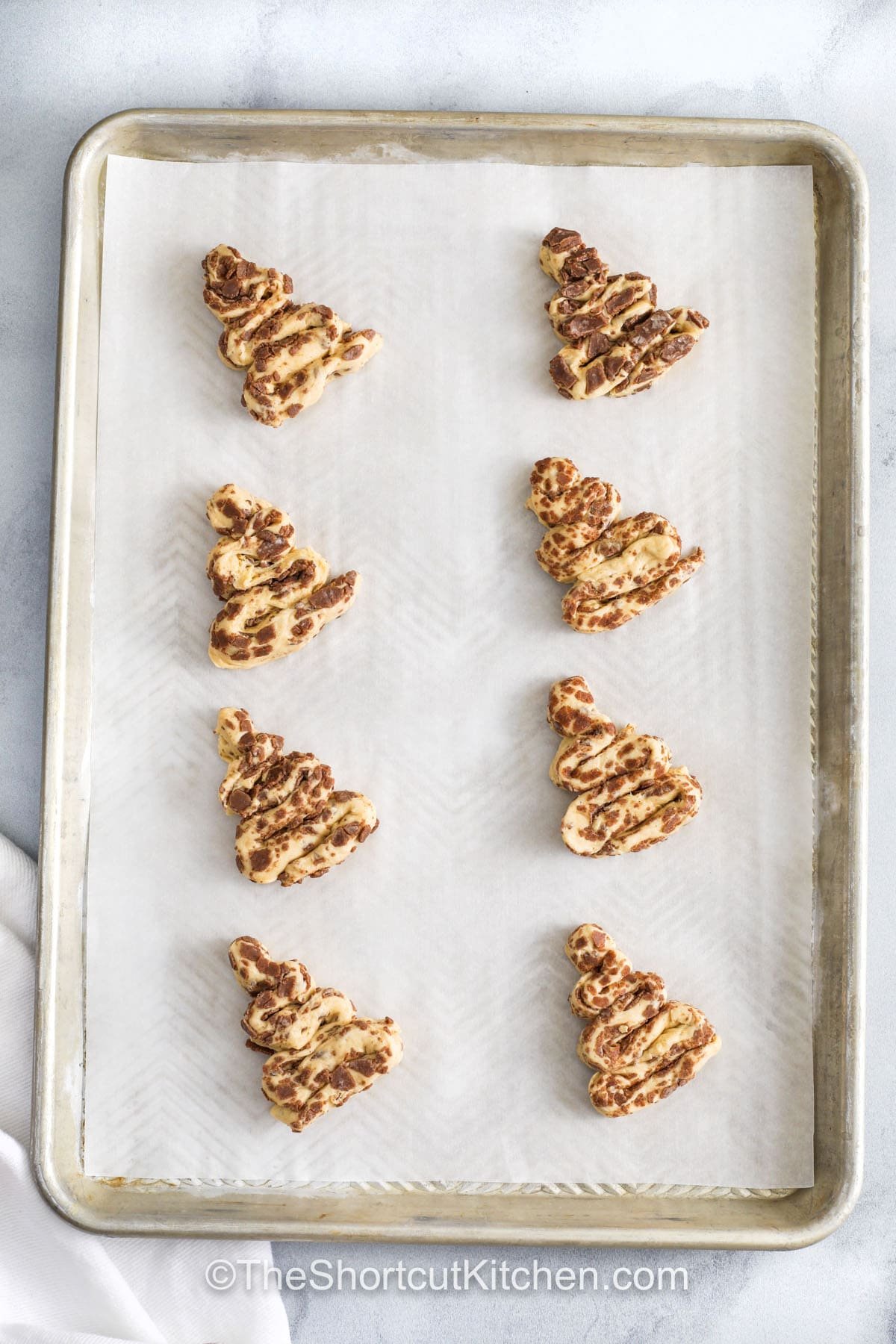 Cinnamon roll Christmas tree treats are quick, fun, and irresistibly tasty for the holiday season. Each soft, fluffy roll is rolled, folded, and baked to perfection before being decorated with icing and festive sprinkles. These sweet, cinnamon-scented pastries are ideal for kids’ parties, brunches, or breakfast spreads, bringing holiday cheer to every bite with minimal prep time. #theshortcutkitchen Cinnamon Roll Christmas Tree on a sheet pan before baking