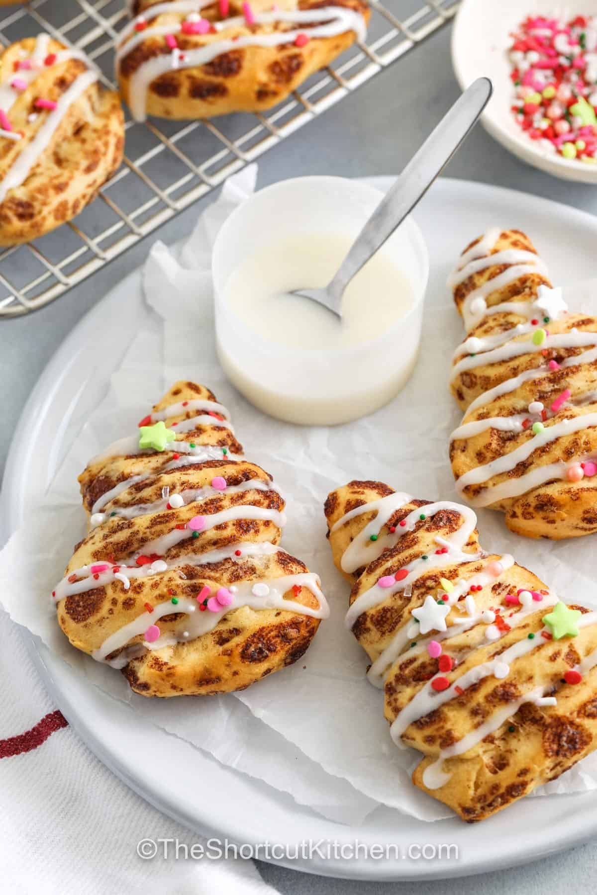 Cinnamon roll Christmas tree treats are a festive, fun twist on classic cinnamon rolls, perfect for holiday mornings. Soft, fluffy, and packed with sweet cinnamon flavor, they are easy to shape into cheerful tree forms and decorated with icing and colorful sprinkles. Ready in under 20 minutes, these playful pastries bring joy to breakfast, brunch, or holiday parties with minimal effort. #theshortcutkitchen close up of Cinnamon Roll Christmas Tree on a plate
