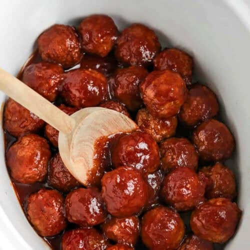 Crockpot Grape Jelly Meatballs in the pot with a wooden spoon