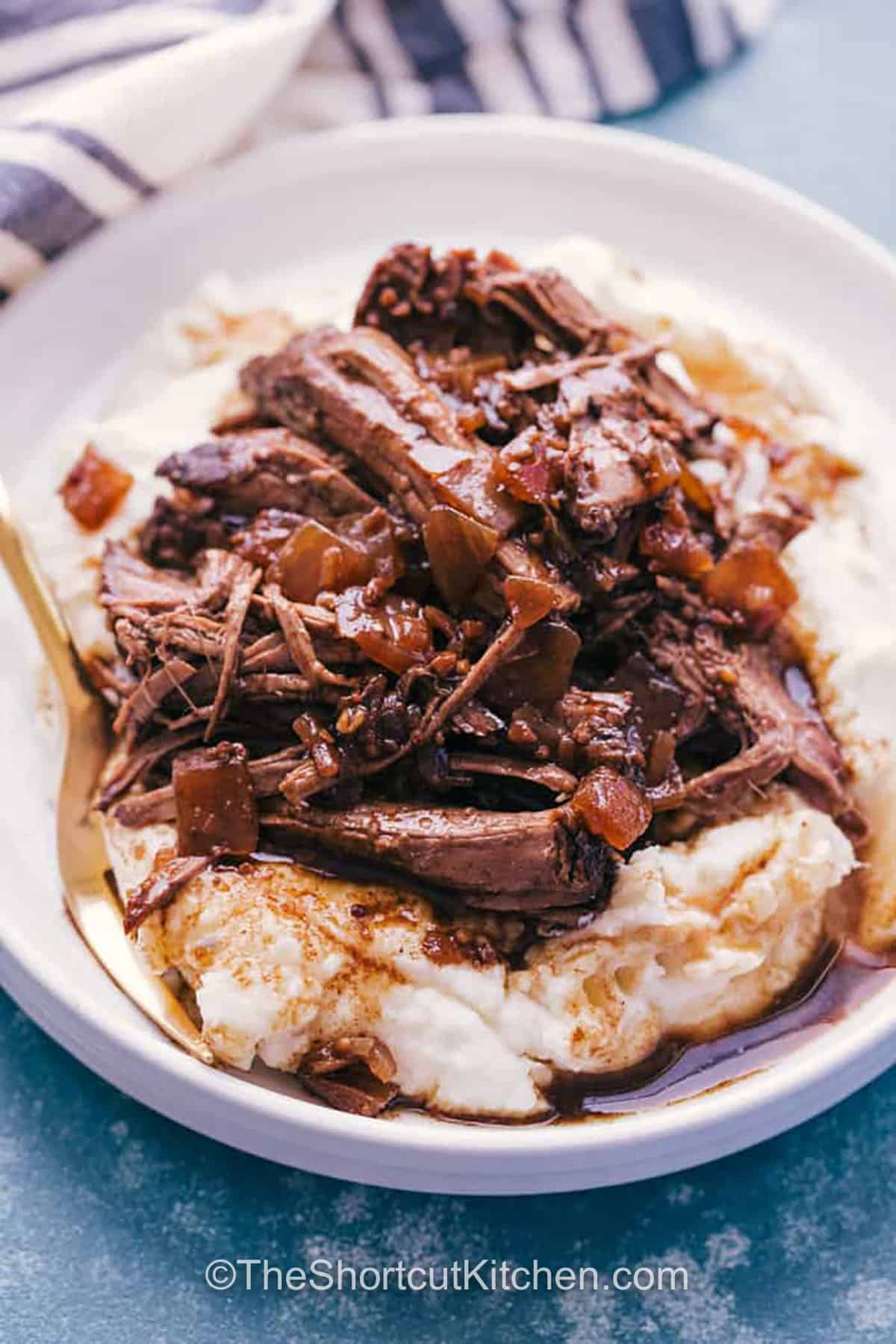 This Crockpot roast beef recipe brings out the best in a chuck or round roast by letting it simmer in broth, balsamic glaze, garlic, and onions until every bite is tender and rich with comforting flavor that suits both weeknight dinner and holiday gatherings. The warm juices soak into the meat to make each serving taste savory and delicious. Pair it with mashed potatoes for a simple meal your family will enjoy. #theshortcutkitchen plated Crockpot Roast Beef Recipe with mashed potatoes