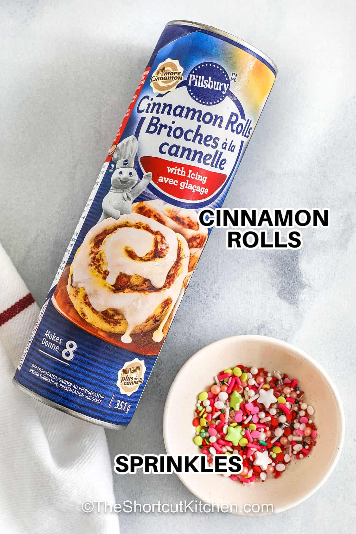 Cinnamon roll Christmas tree treats bring holiday magic to your breakfast table with ease. Soft, tender, and full of cinnamon-sugar flavor, these rolls are folded into tree shapes and finished with icing and festive sprinkles. They are simple to make, fun to decorate, and perfect for creating memorable holiday mornings that are both sweet and joyful. #theshortcutkitchen cinnamon rolls and sprinkles with labels to make Cinnamon Roll Christmas Tree