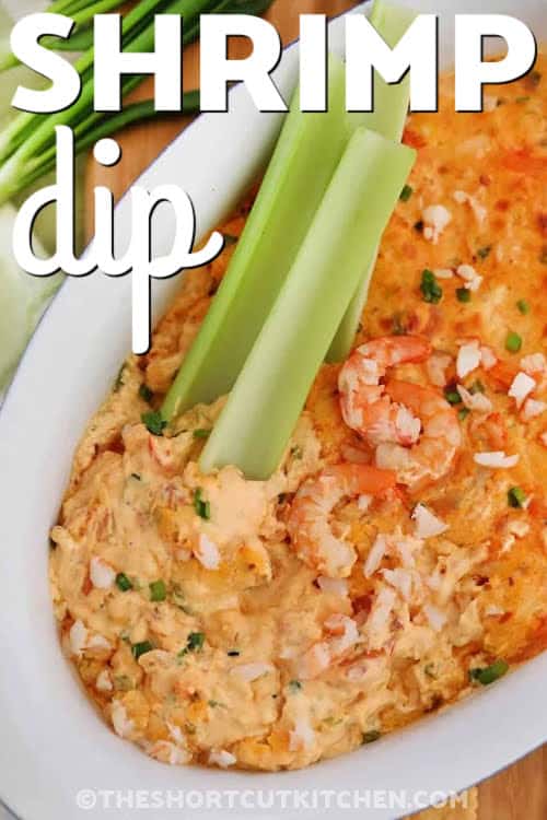 This creamy shrimp dip is made with tender chopped shrimp, rich cream cheese, and sharp cheddar for a warm, flavorful appetizer. This dip is perfect for New Year’s Eve and Super Bowl parties. Everything mixes easily in one bowl before baking into a bubbly, golden dip. It pairs well with crackers, chips, or crisp vegetables. It’s simple to prepare, easy to transport, and a reliable crowd favorite for any gathering. #theshortcutkitchen shrimp dip in a bowl with two celery sticks and writing