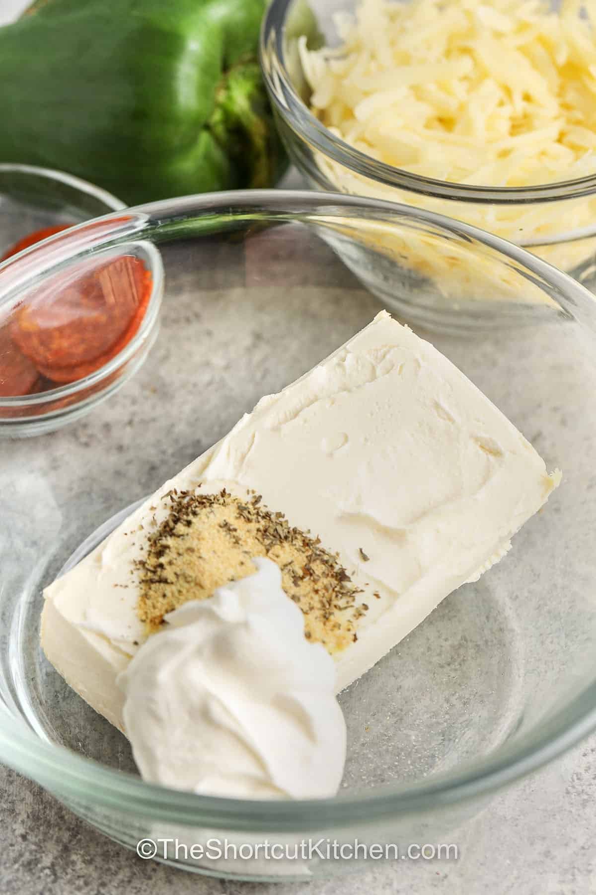 Make this pizza dip recipe for the best easy appetizer full of rich, creamy flavor. Hot and bubbly from the oven, it’s layered with sauce, garlic, cheese, and pepperoni. Each bite is cheesy, comforting, and perfect for sharing. This simple dip is a favorite at family gatherings and parties. Serve it warm with crackers or toasted bread for a snack that tastes like pizza perfection. #theshortcutkitchen adding seasonings to cream cheese and sour cream to make Pizza Dip Recipe