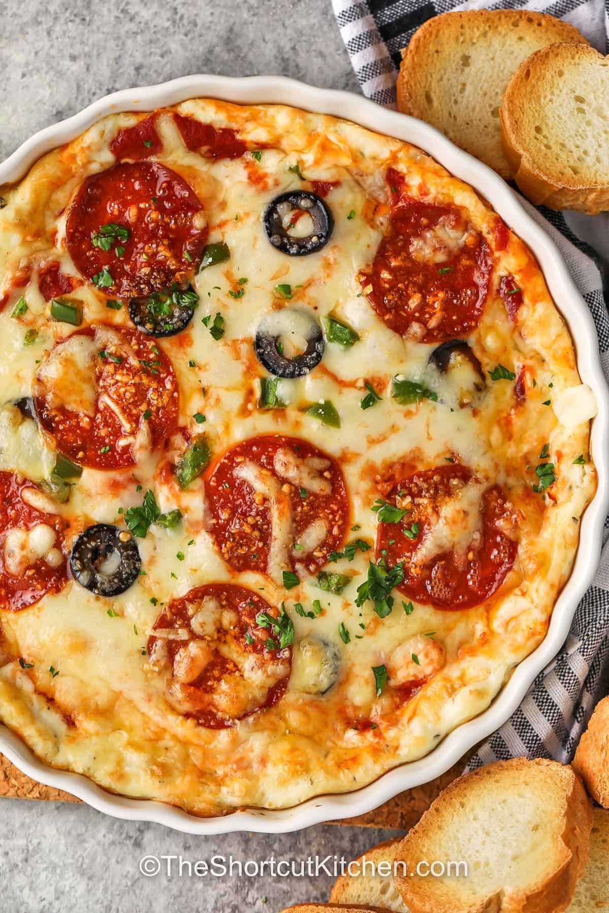 This pizza dip recipe is the best way to bring everyone to the table. It’s creamy, cheesy, and packed with flavor from garlic, sauce, and pepperoni. You can make it in one dish and serve it hot and bubbly straight from the oven. It’s simple, easy, and always a hit with kids and adults alike. Every scoop tastes like your favorite pizza in dip form, perfect for any gathering or cozy night in. #theshortcutkitchen plated Pizza Dip Recipe with bread pieces