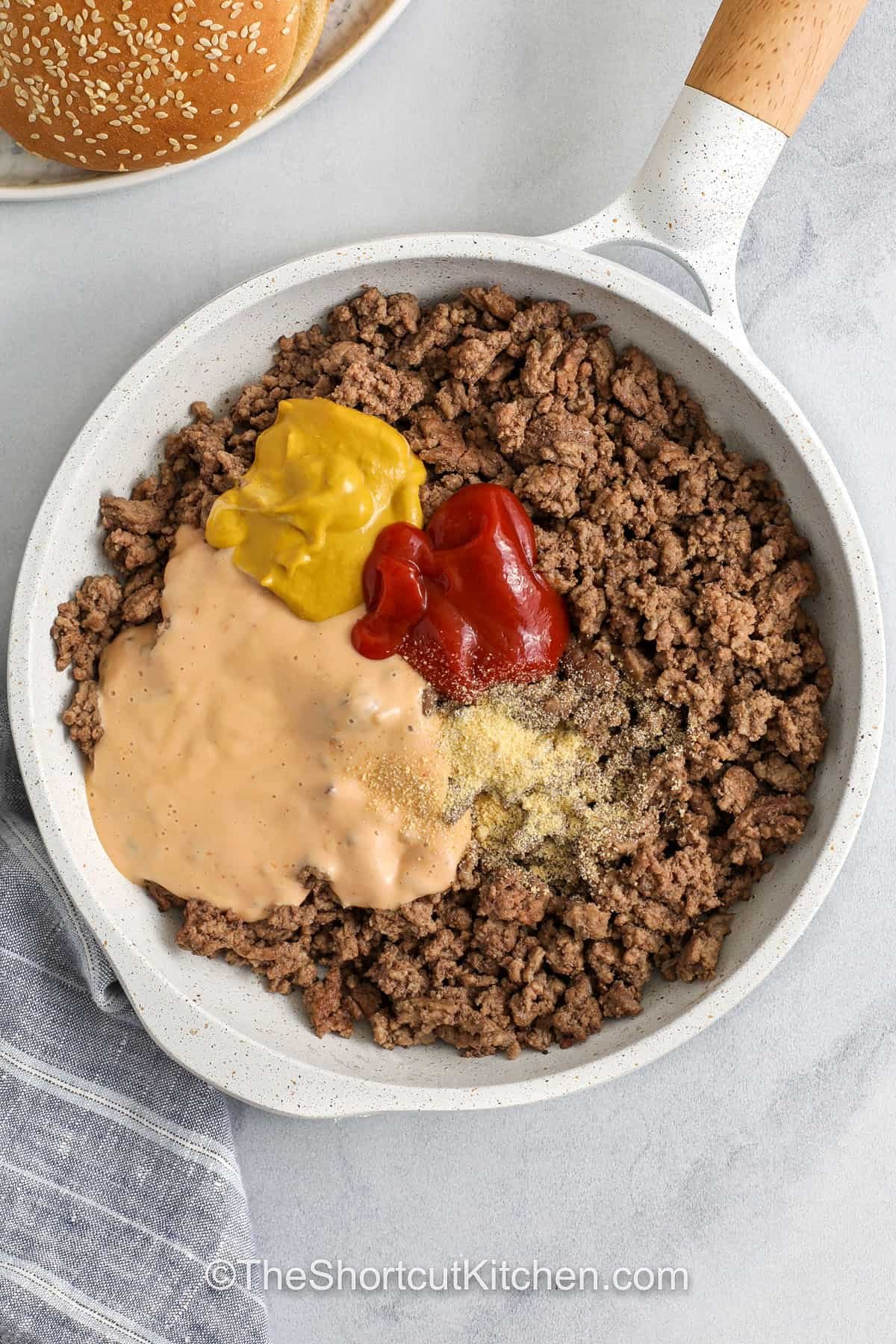 Skip the drive-thru and make Big Mac Sloppy Joes at home in one skillet. Ground beef cooks up fast, then gets tossed in a tangy, creamy sauce made with Thousand Island dressing, ketchup, and mustard. Serve on hamburger buns with pickles, shredded lettuce, and melty American cheese. This copycat Big Mac Sloppy Joes recipe is perfect for busy weeknights and game day. #theshortcutkitchen big mac sloppy joes in a pan with ingredients