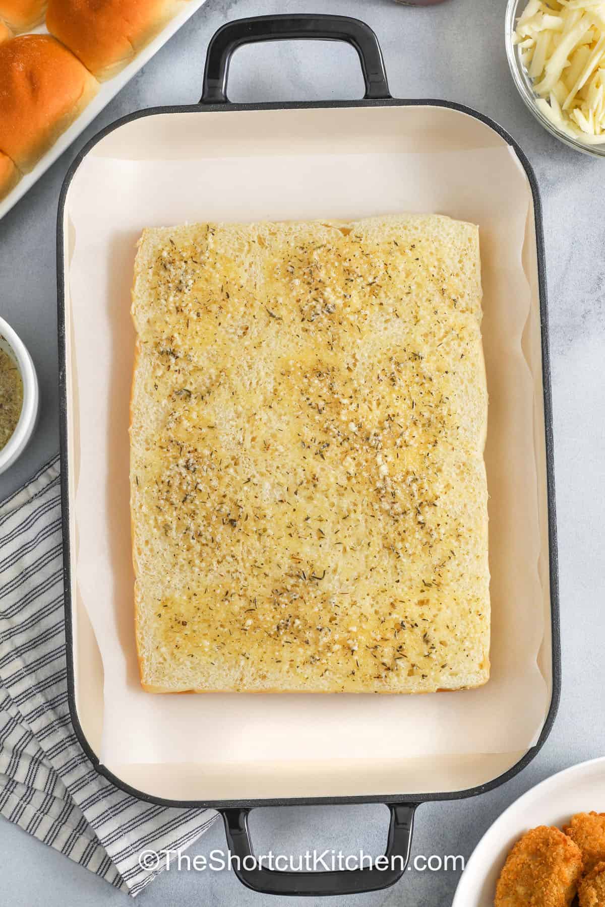 Easy chicken parm sliders are a 9×13-pan win. Crispy frozen chicken nuggets and marinara sauce and mozzarella cheese layered on Hawaiian rolls, finished with garlic butter, Italian seasoning, and parmesan. Bake until the cheese melts and the tops brown. These chicken nugget parmesan sliders are perfect for parties, after-school snacks, or a fast weeknight dinner. #theshortcutkitchen chicken parm sliders with garlic butter in a pan